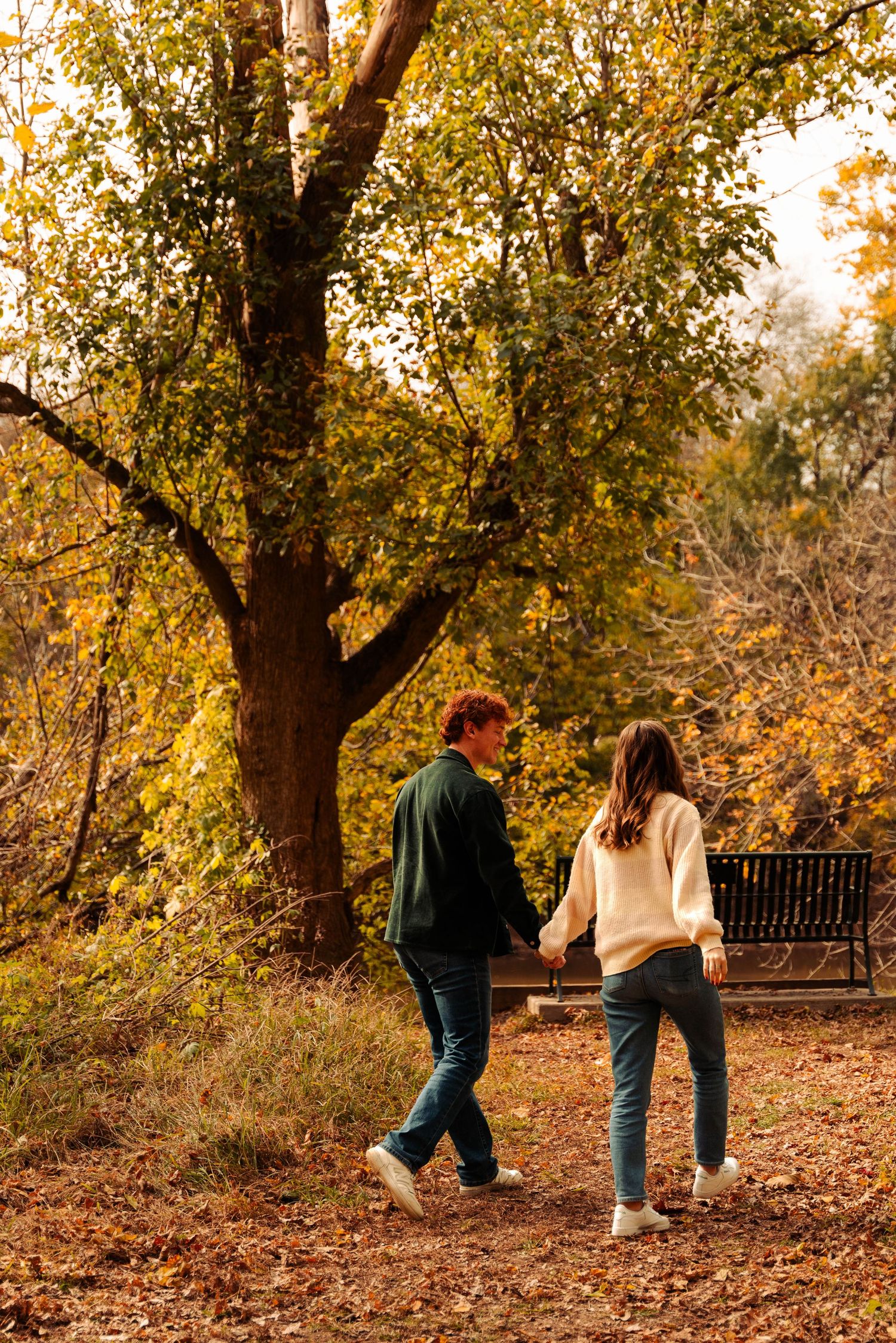 Two people walking hand-in-hand on a path surrounded by vibrant autumn foliage.