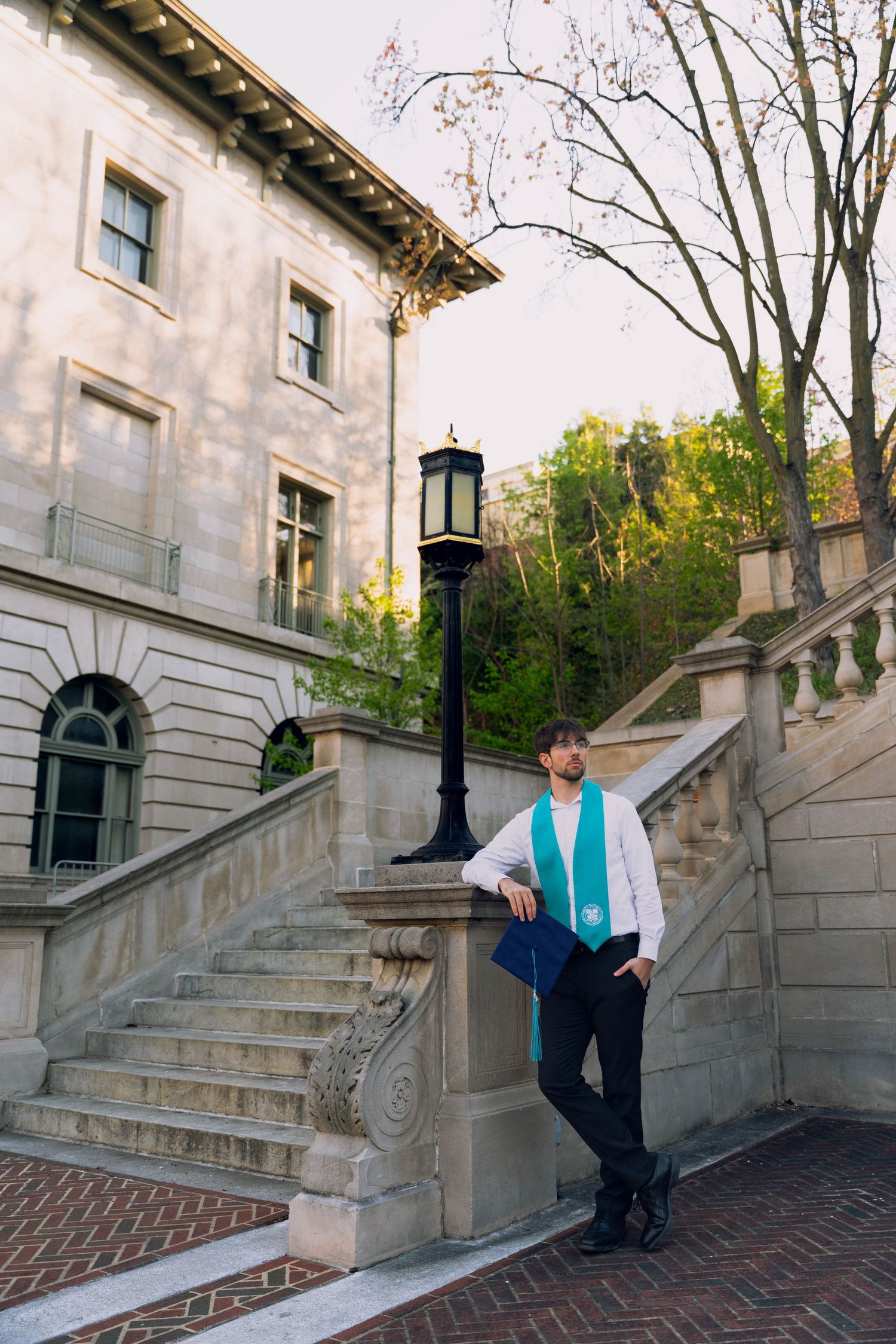 A person standing on stone steps in front of a historic building with a lamp post and trees in the background.