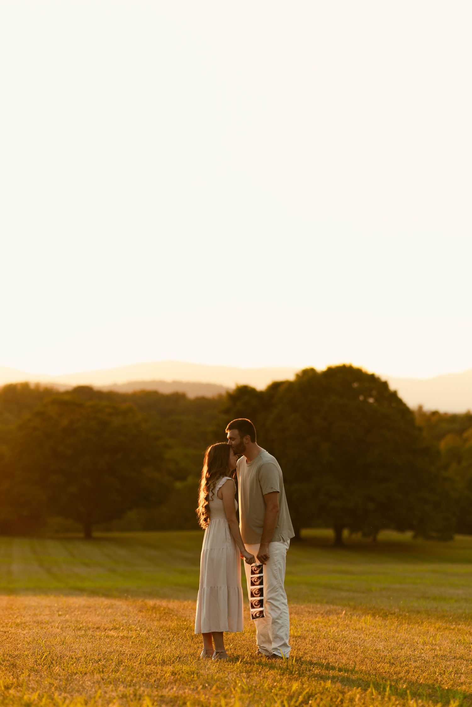 Couple standing together in golden field during sunset.