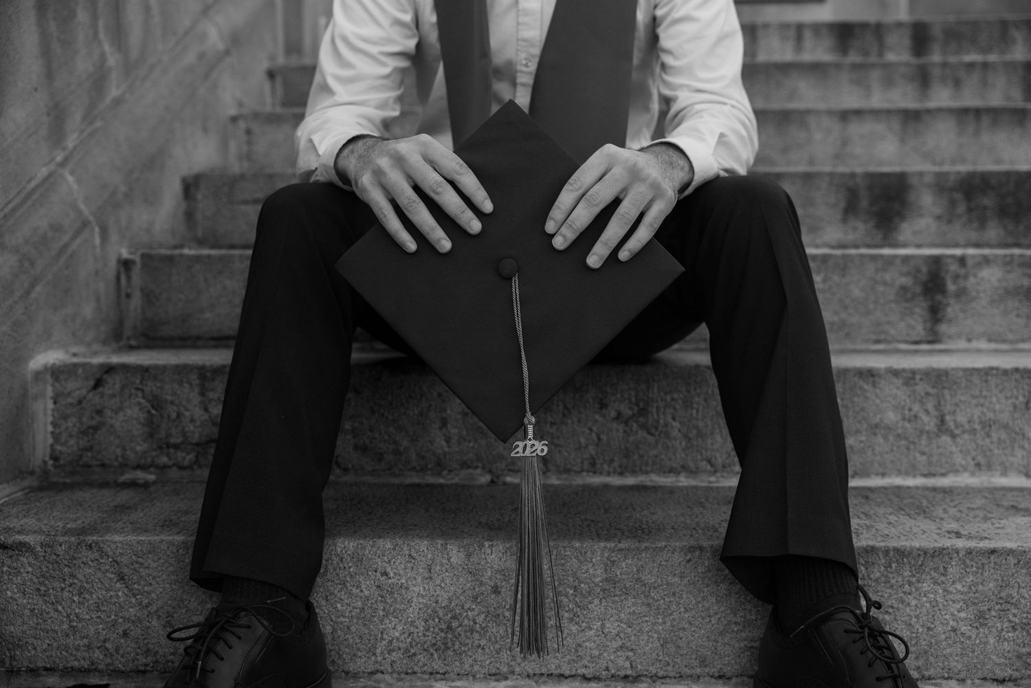 A black and white image shows a person sitting on stone steps, with their hands clasped in front of them.