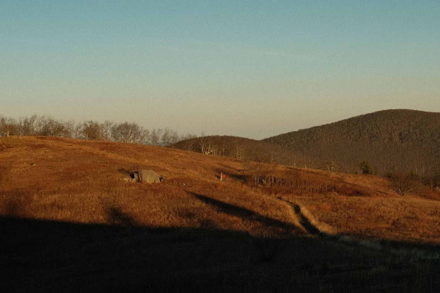 A scenic rural landscape with rolling hills, trees, and a clear sky in the distance.