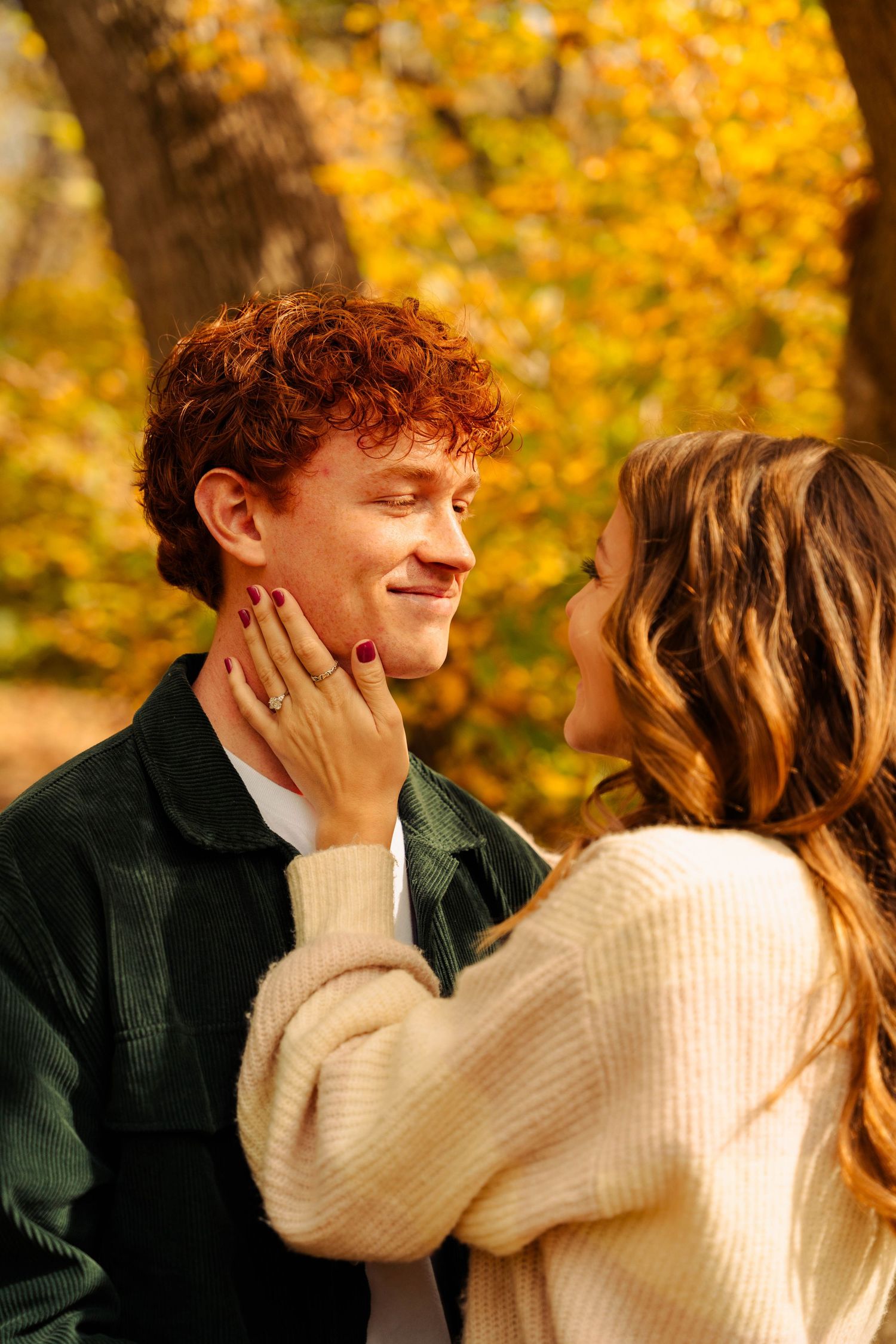 A couple shares an intimate moment among fall foliage with warm lighting.