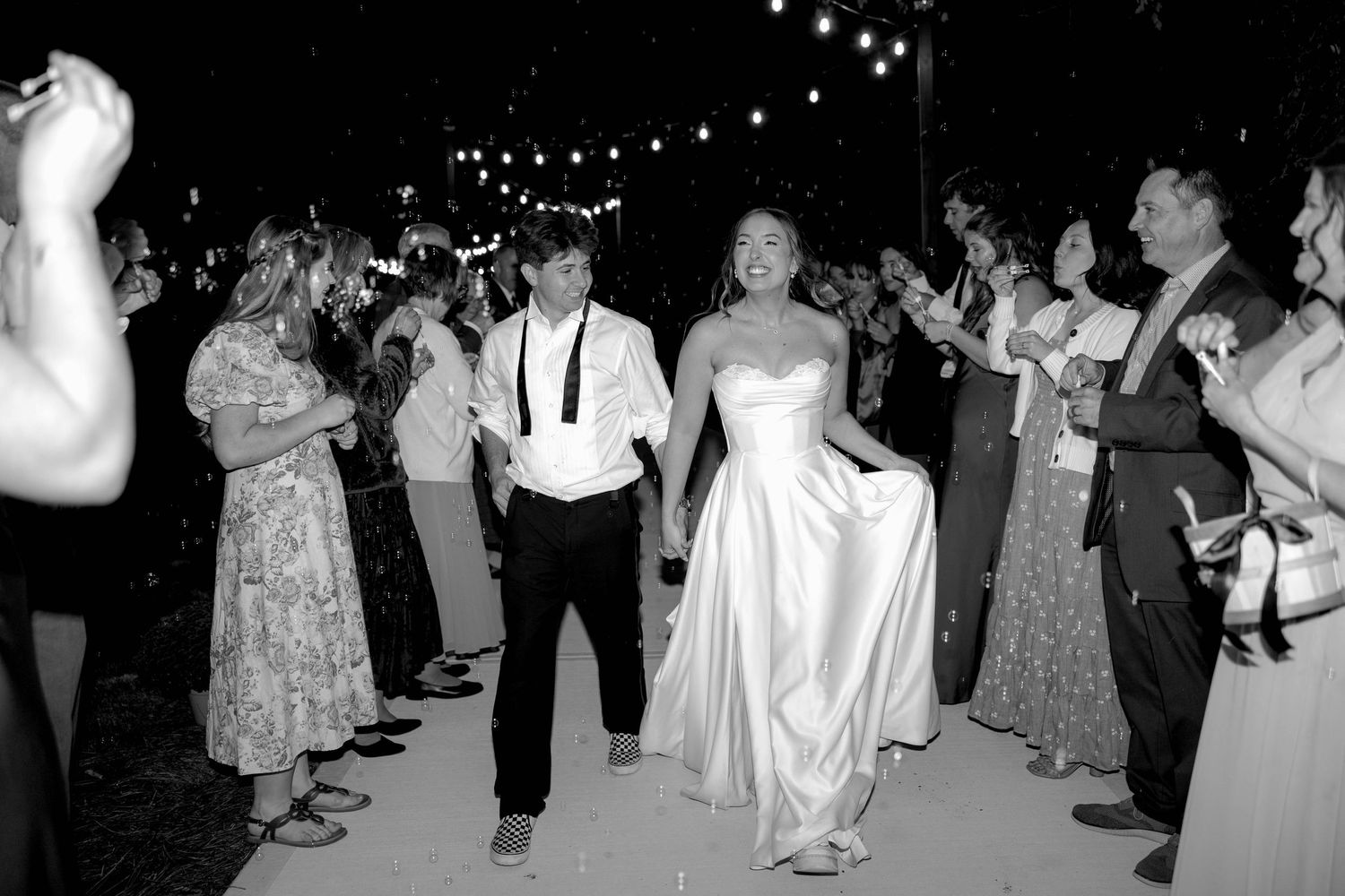 Black and white photo of bride and groom making grand exit through cheering wedding guests outdoors.