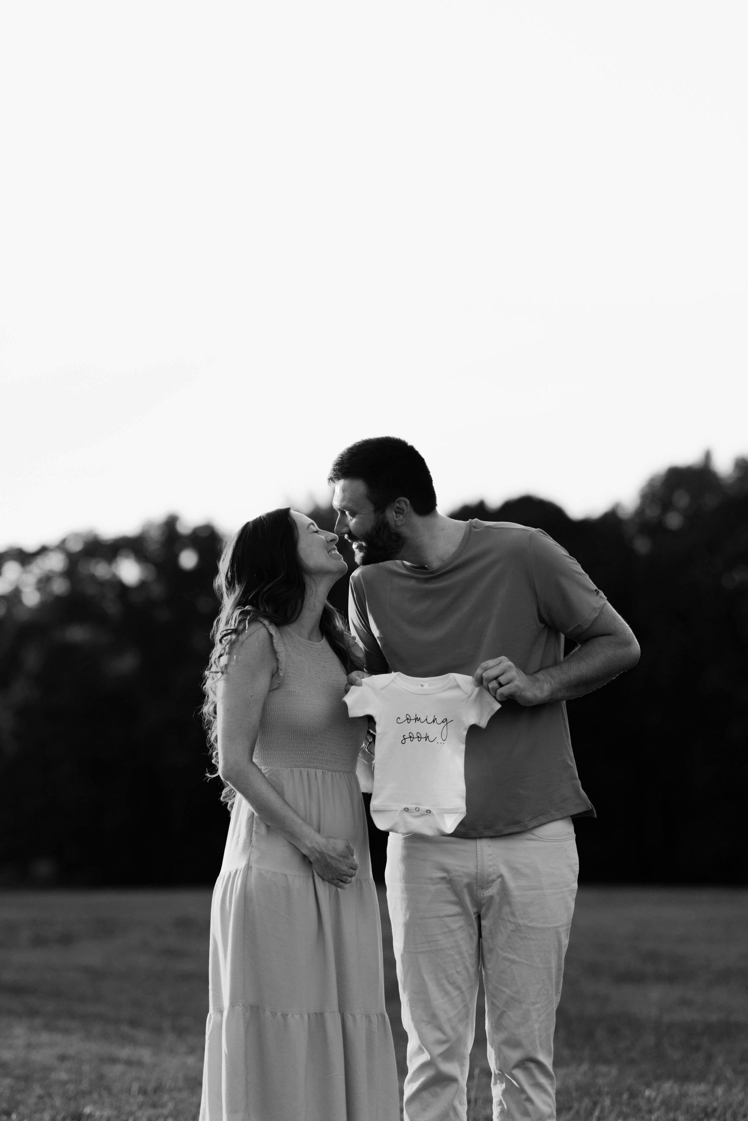 Silhouetted couple holding baby clothes during sunset pregnancy announcement shoot.