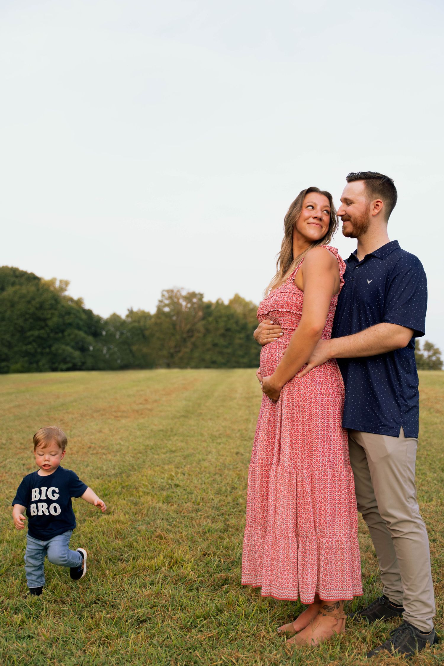 Pregnancy announcement photoshoot in a grassy field at sunset.