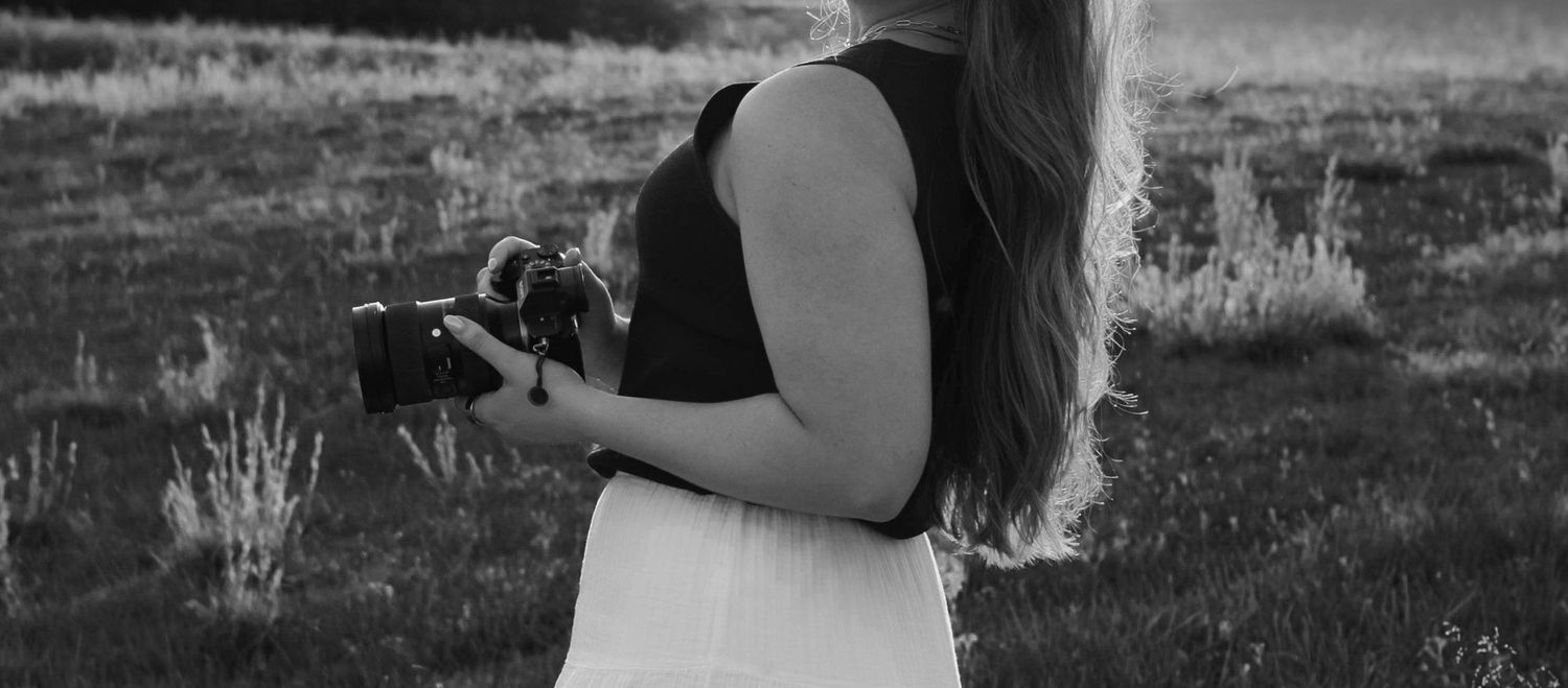 Woman holding a camera in a field, black and white photography outdoor portrait.