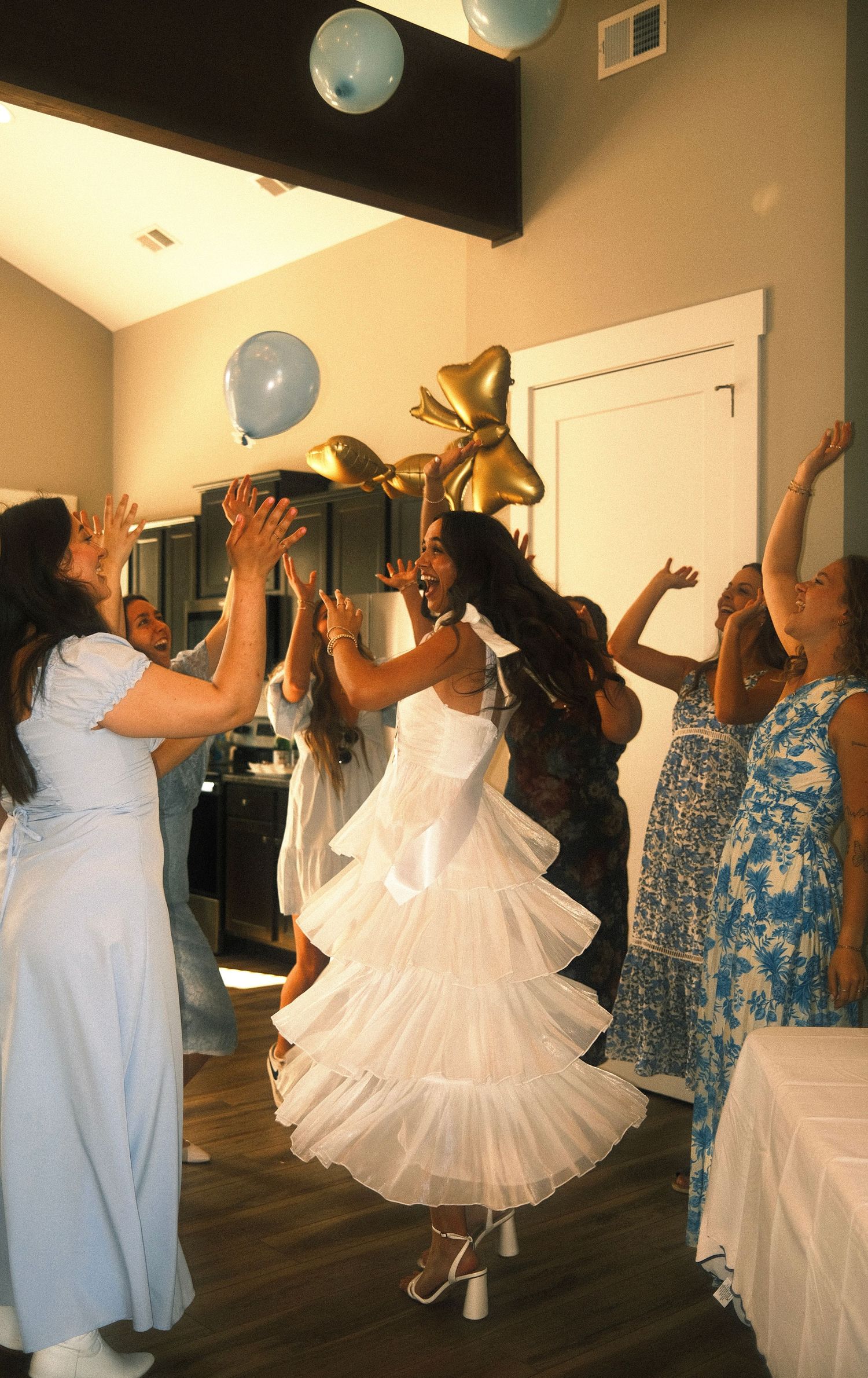 A group of people, including a bride in a white dress, are dancing and celebrating at what appears to be a wedding reception.
