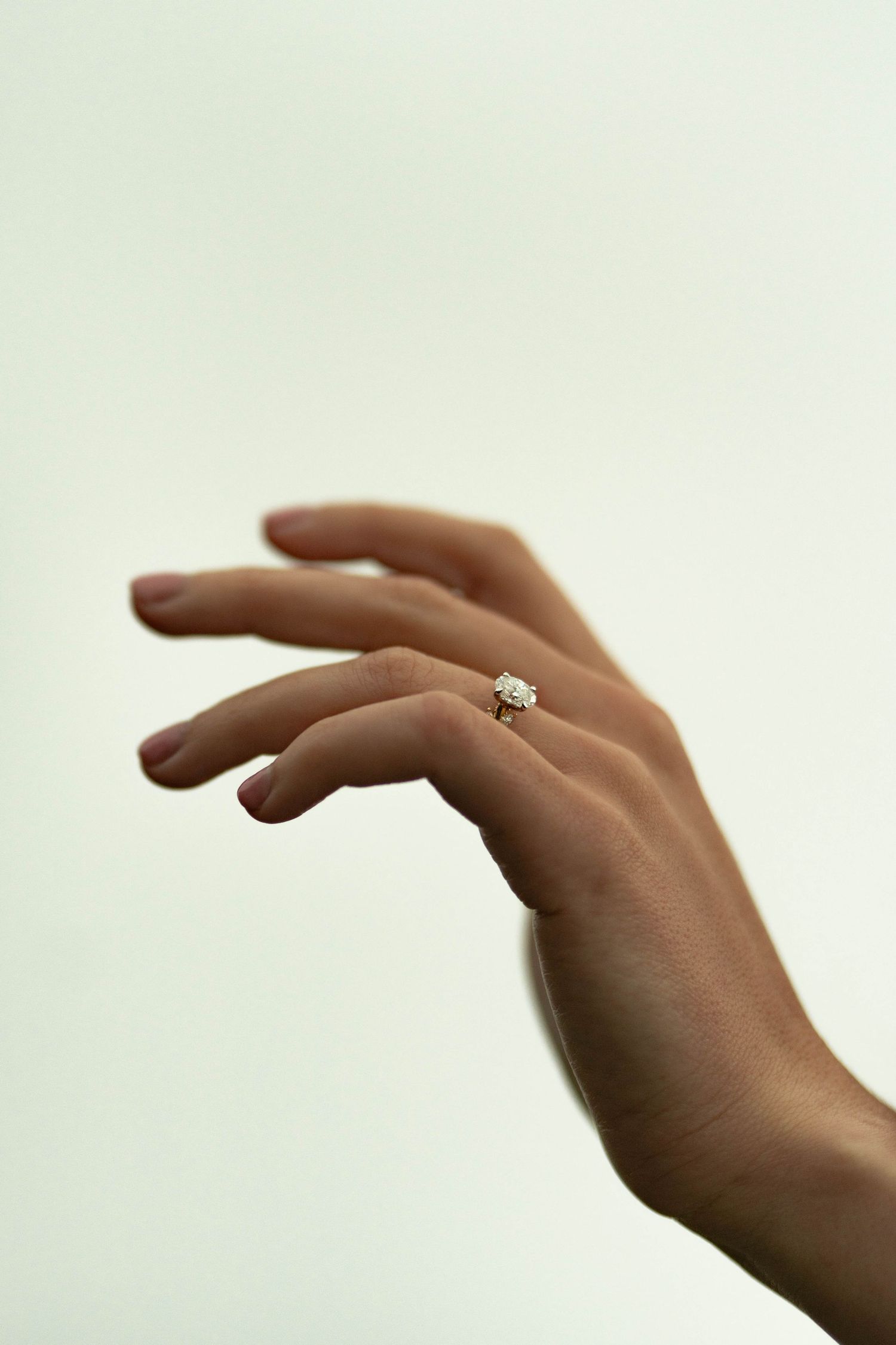 Elegant hand wearing a solitaire diamond engagement ring on ring finger against a soft white background.