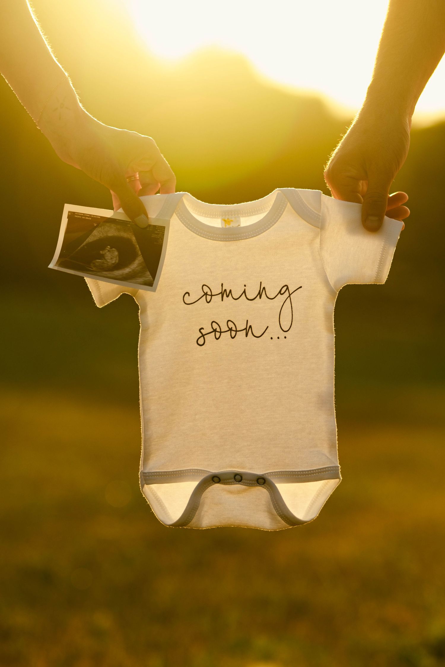 Baby onesie with handwritten text hanging on clothesline at sunset.