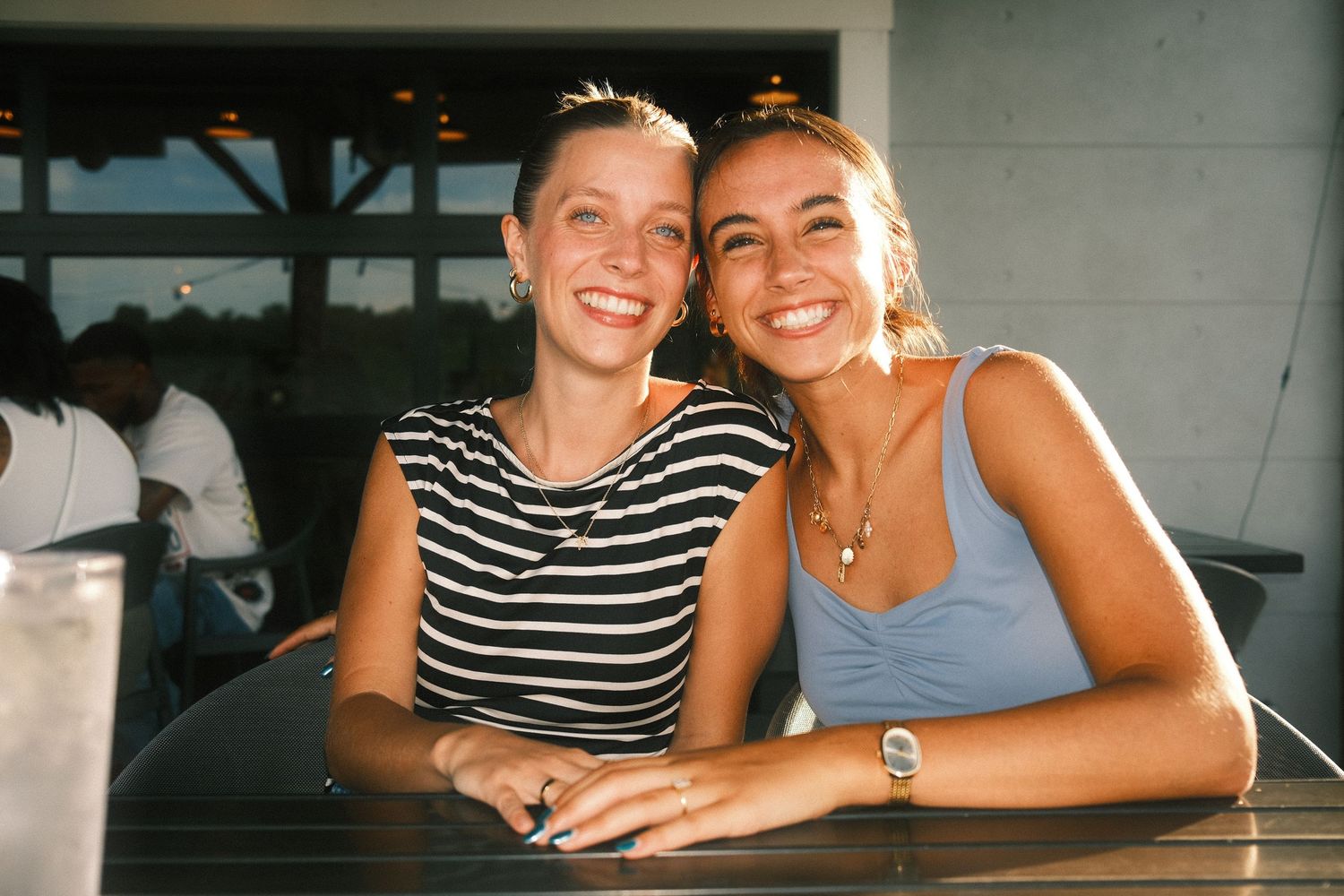 Two smiling young women, one wearing a striped shirt and the other a blue tank top, posing together.