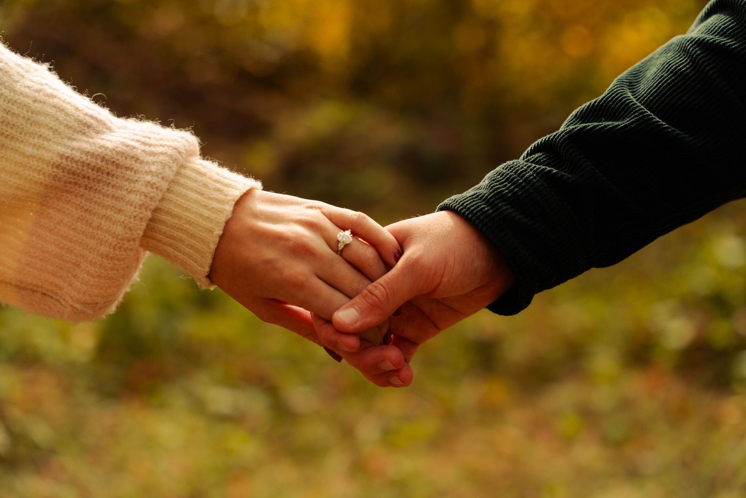 Hands reaching toward each other against a blurred autumn background.