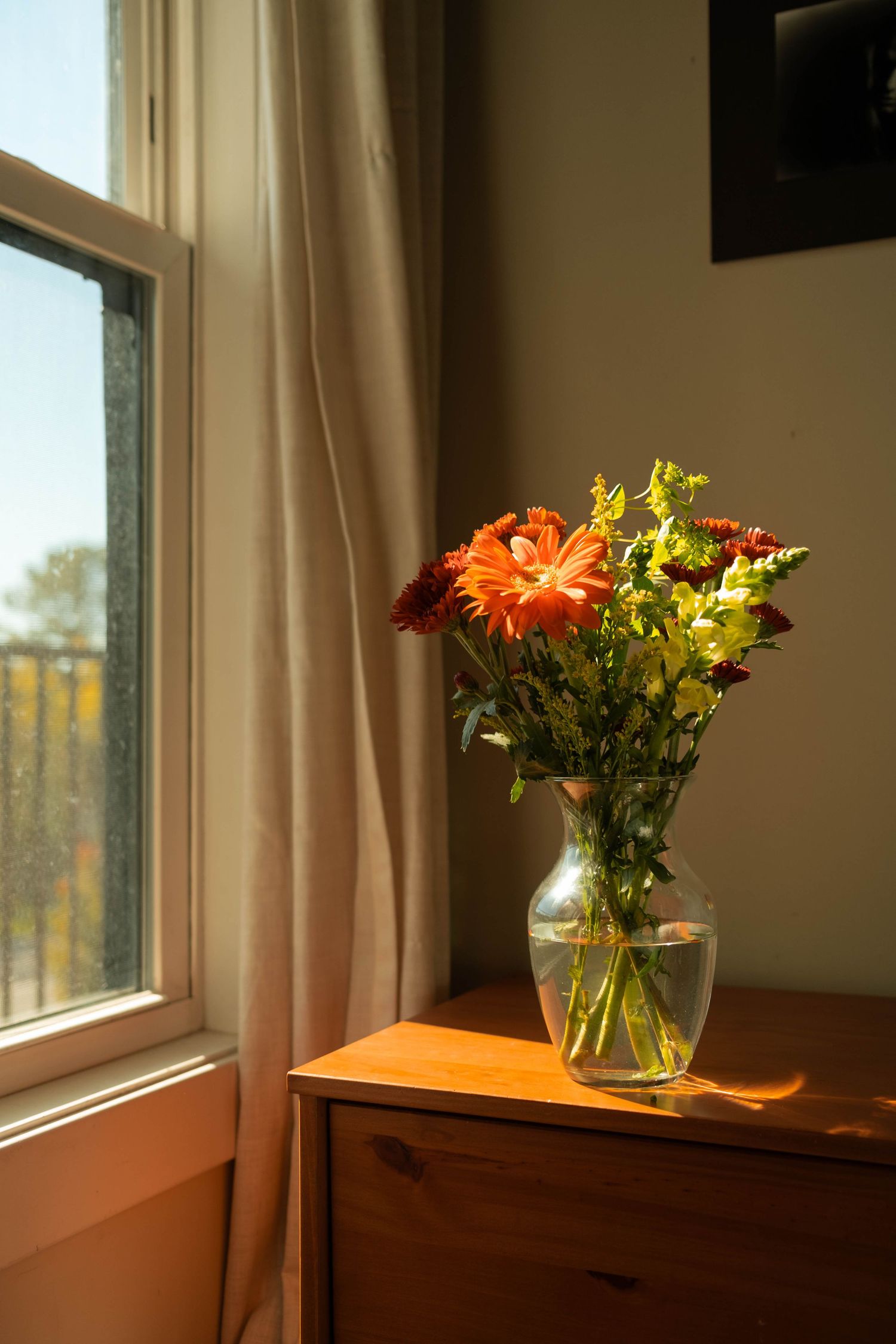 A vase of colorful flowers sits on a wooden dresser near a window, creating a warm and cozy atmosphere.