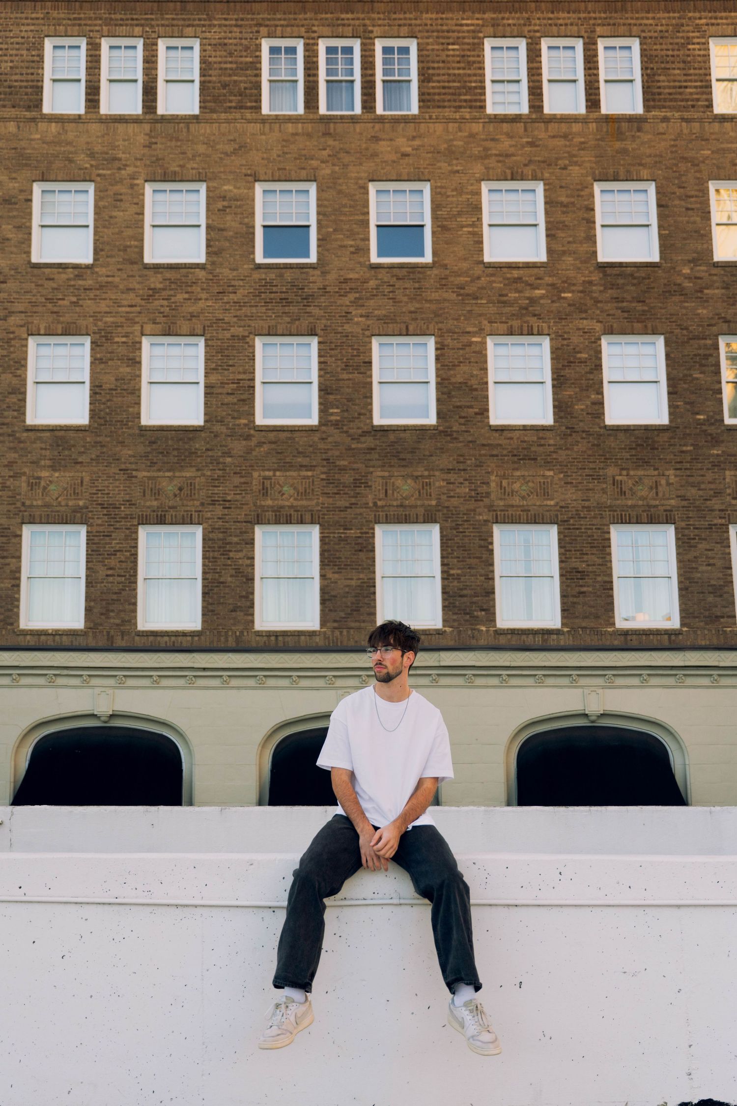 A person sitting on a concrete ledge in front of a brick building with many windows.