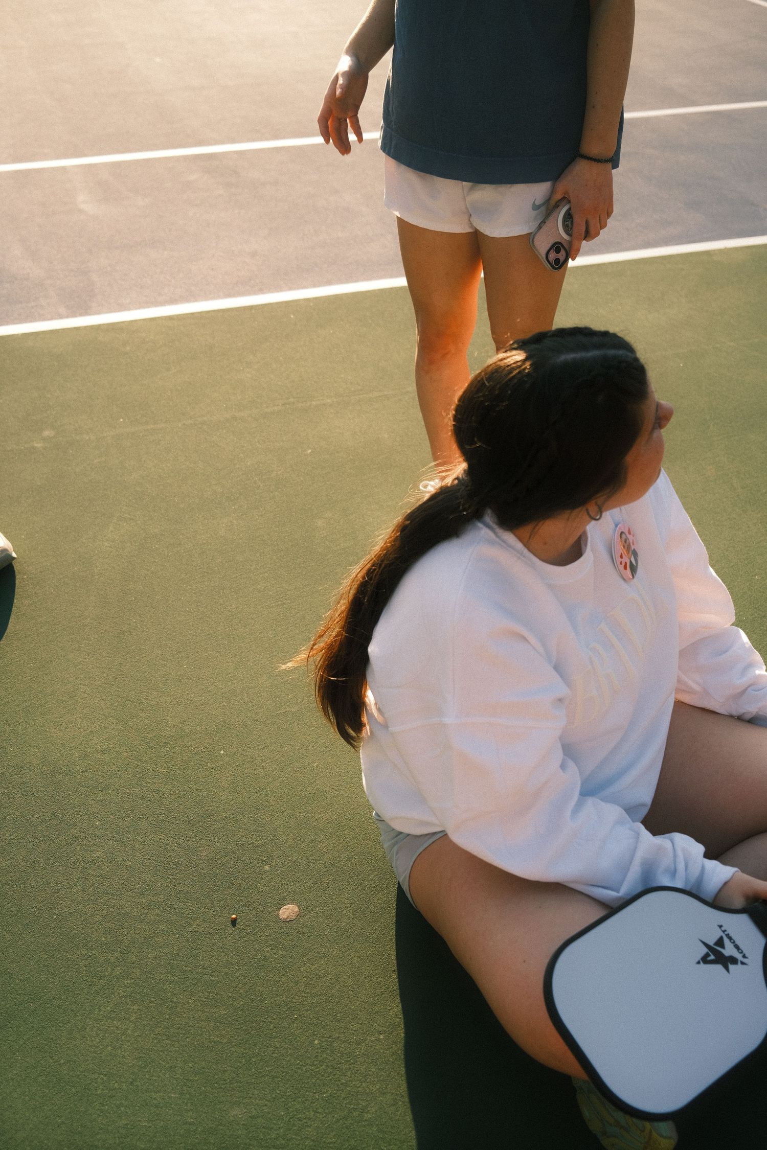 Two people, a man and a woman, are standing on a tennis court, with the woman sitting on the ground and the man standing above her.