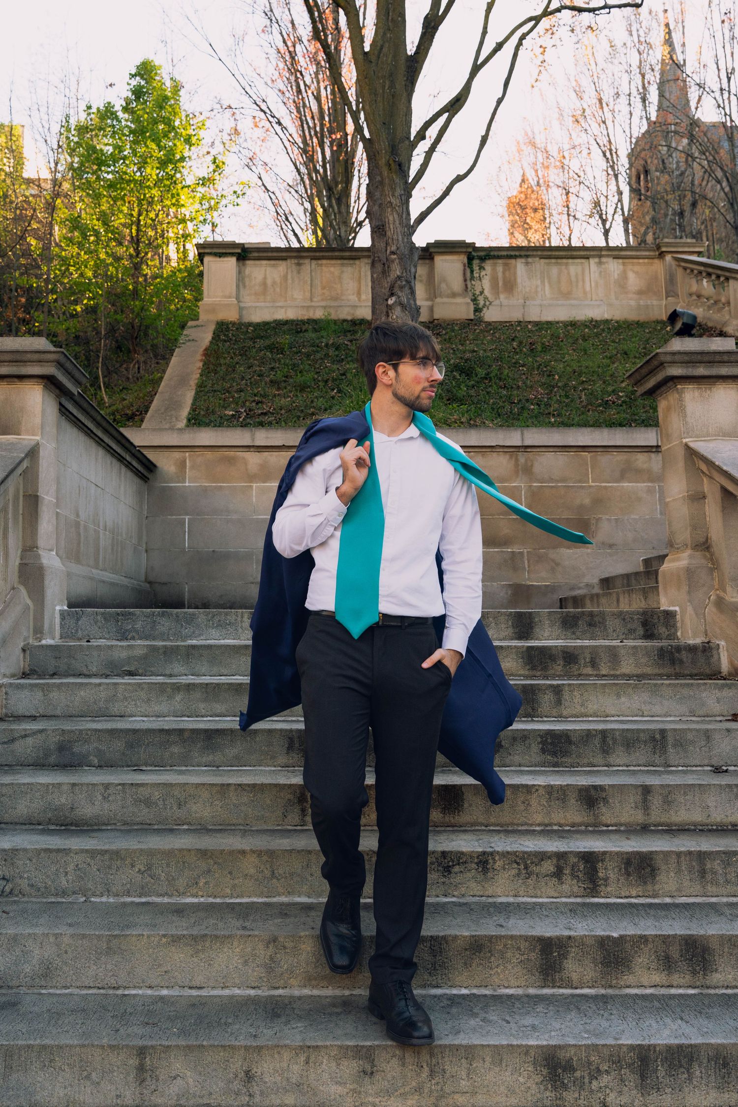 A young man wearing a blue jacket and backpack walking up stone steps in an urban outdoor setting.