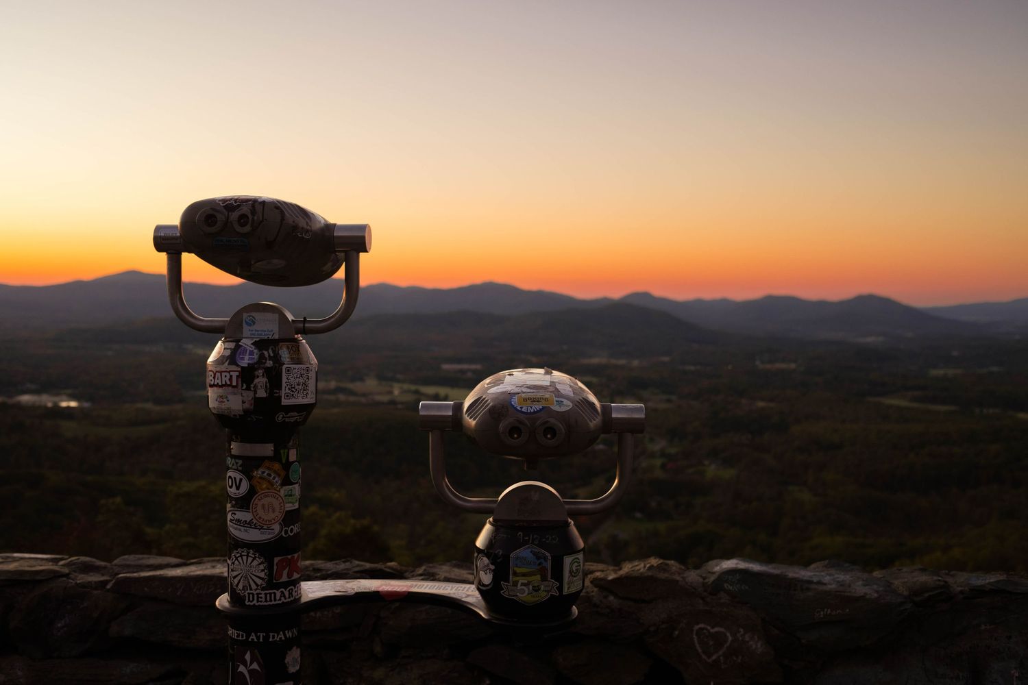 A telescope silhouetted against a colorful sunset sky, with mountains in the distance.