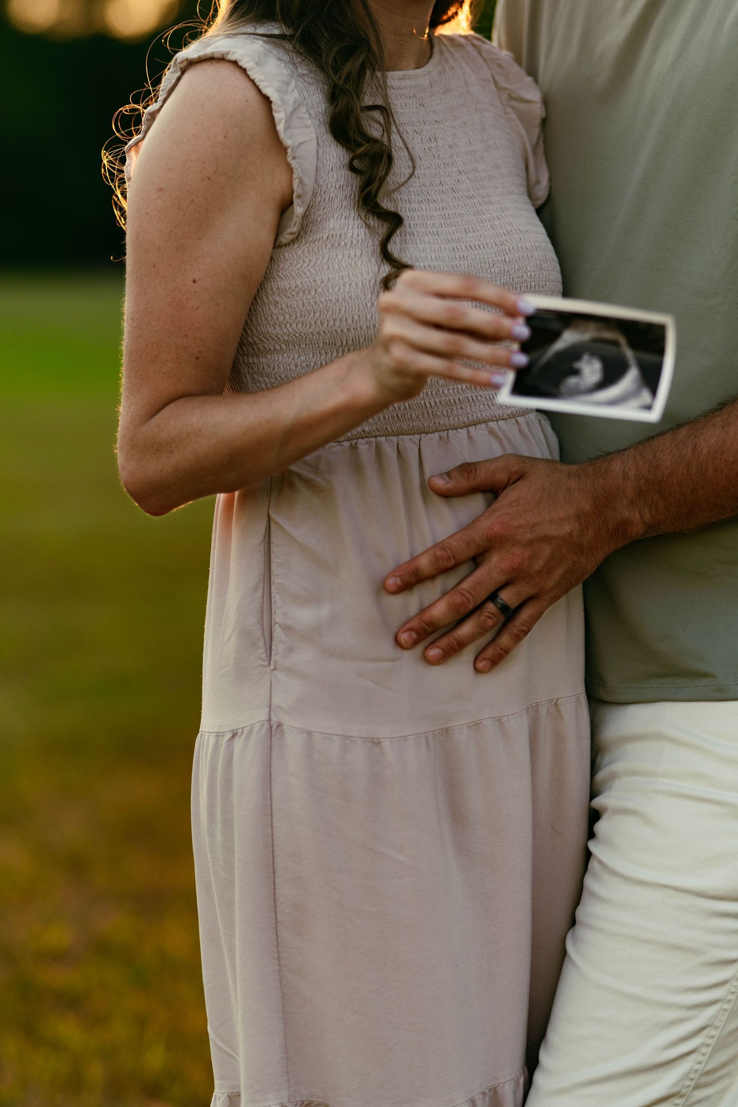 Couple embracing with hands on pregnant belly in outdoor setting.
