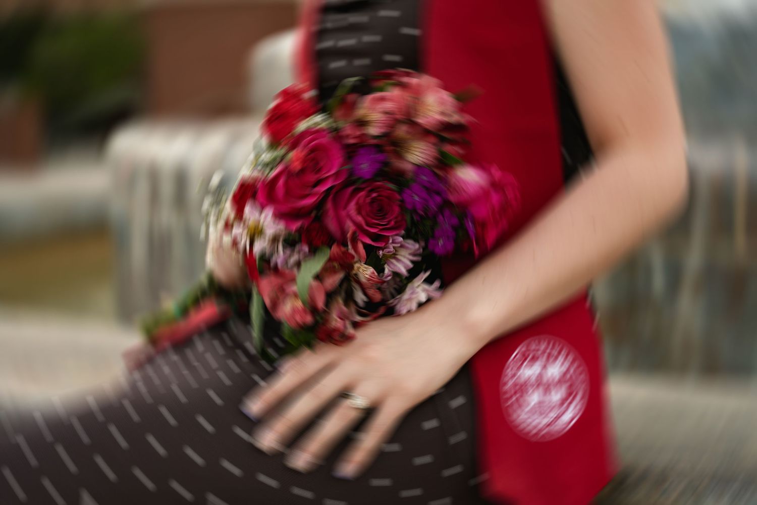 Graduate holding a vibrant red and pink floral bouquet while wearing a red graduation sash.
