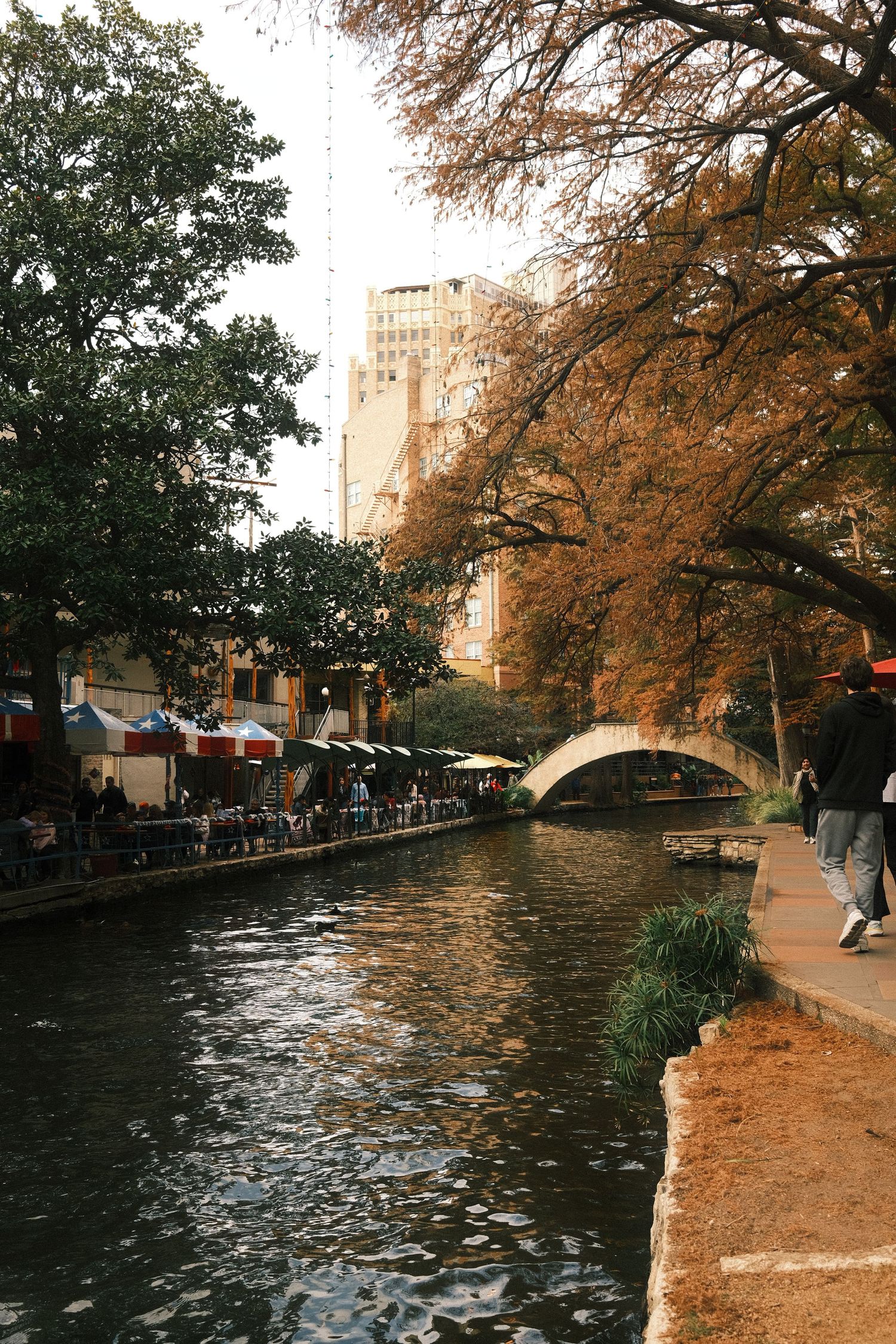 A scenic view of a canal in a city, with trees lining the banks and pedestrians walking along the waterway.