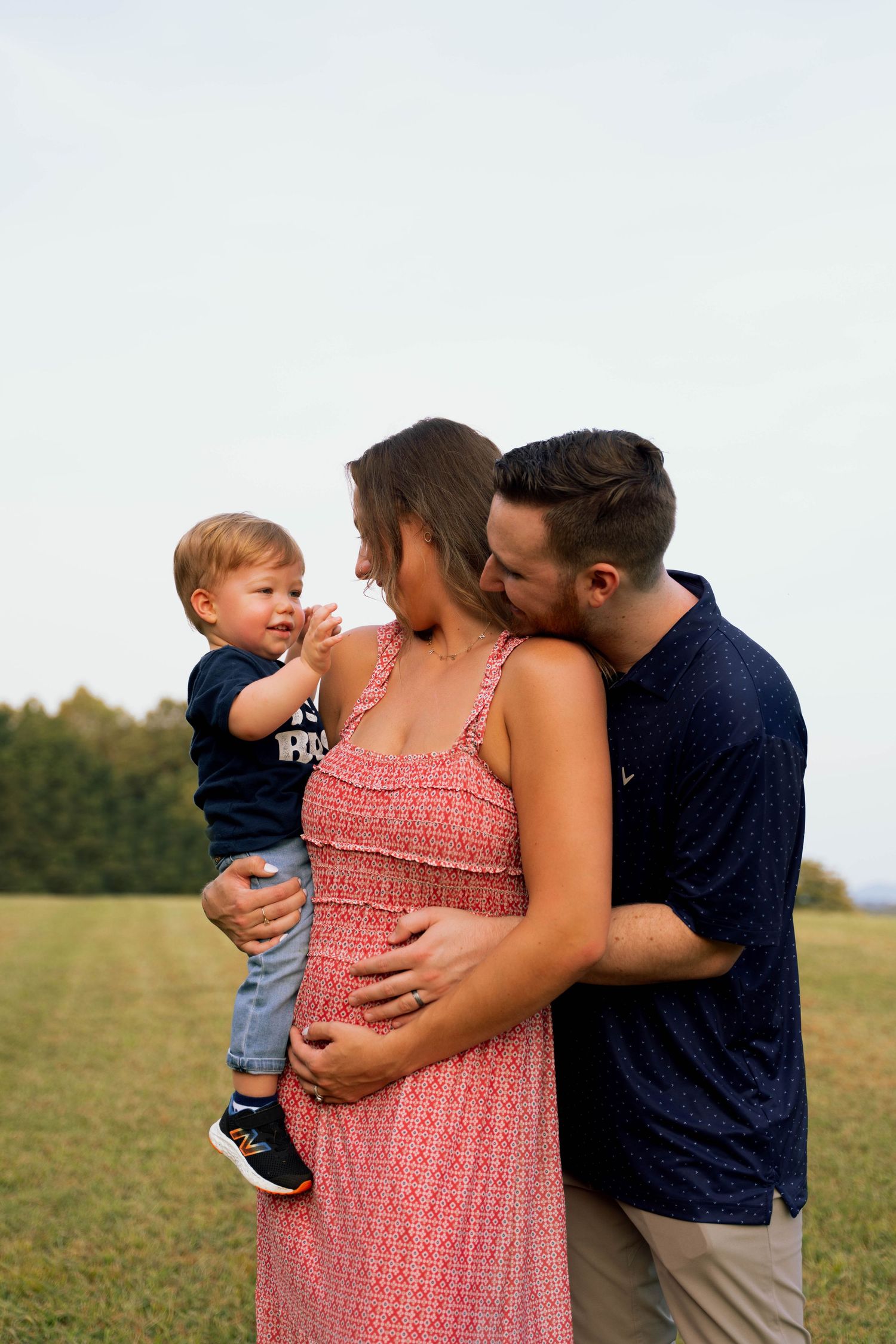 A young family enjoying a moment together in a grassy field, with a mother holding a baby and a father embracing them.
