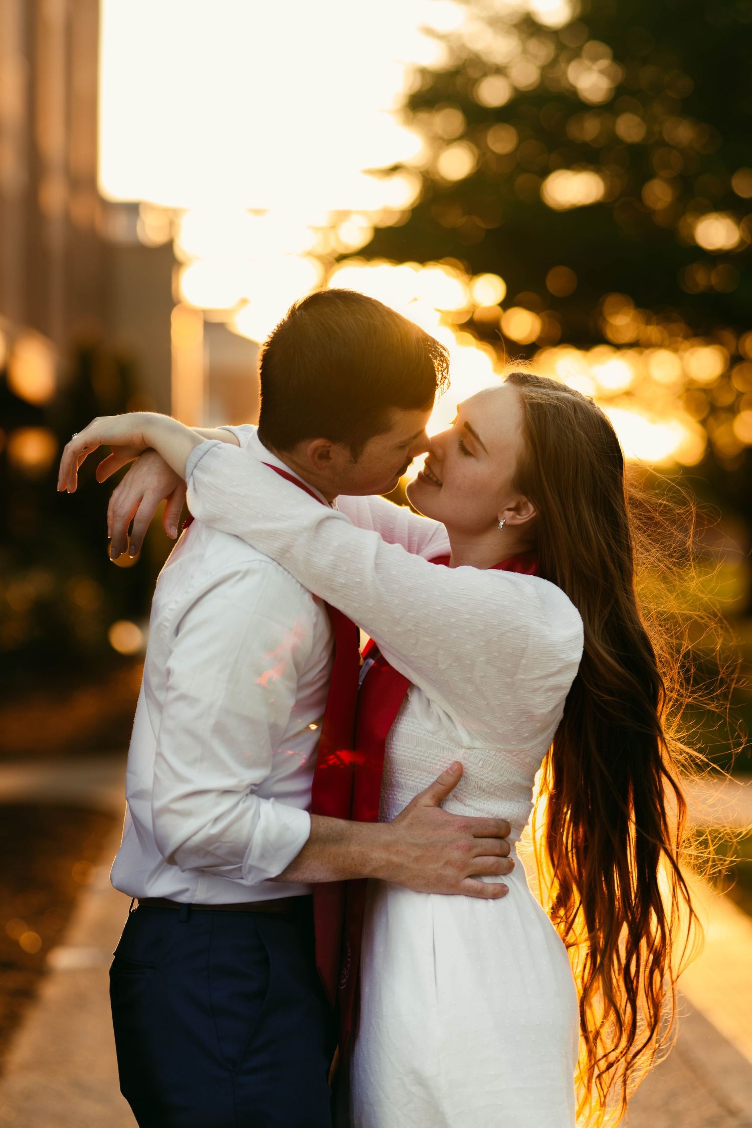 A couple embraces in a romantic sunset moment with golden bokeh lighting and long flowing hair in the breeze.