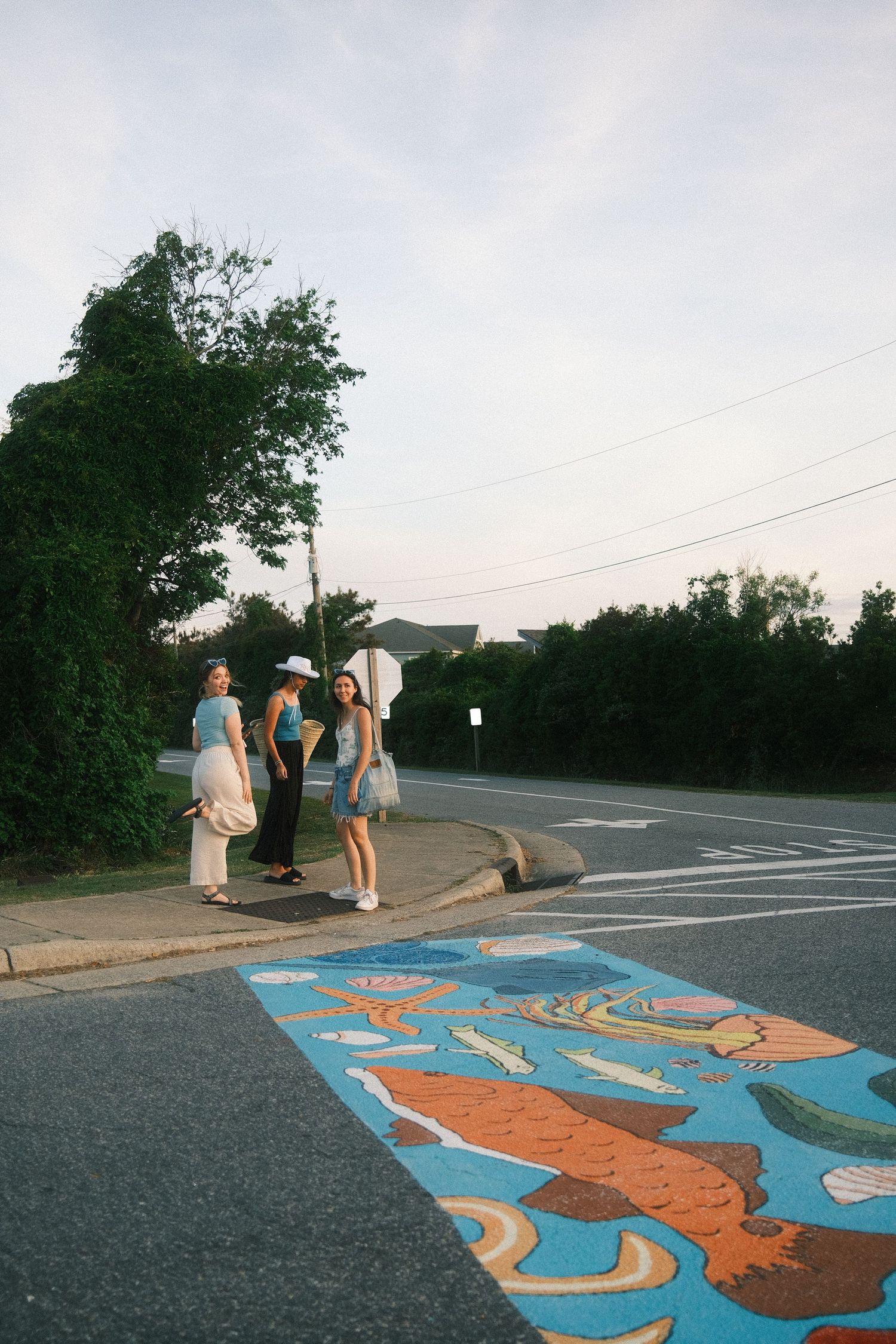 The image shows a group of people walking on a colorful, patterned sidewalk near a road with trees in the background.