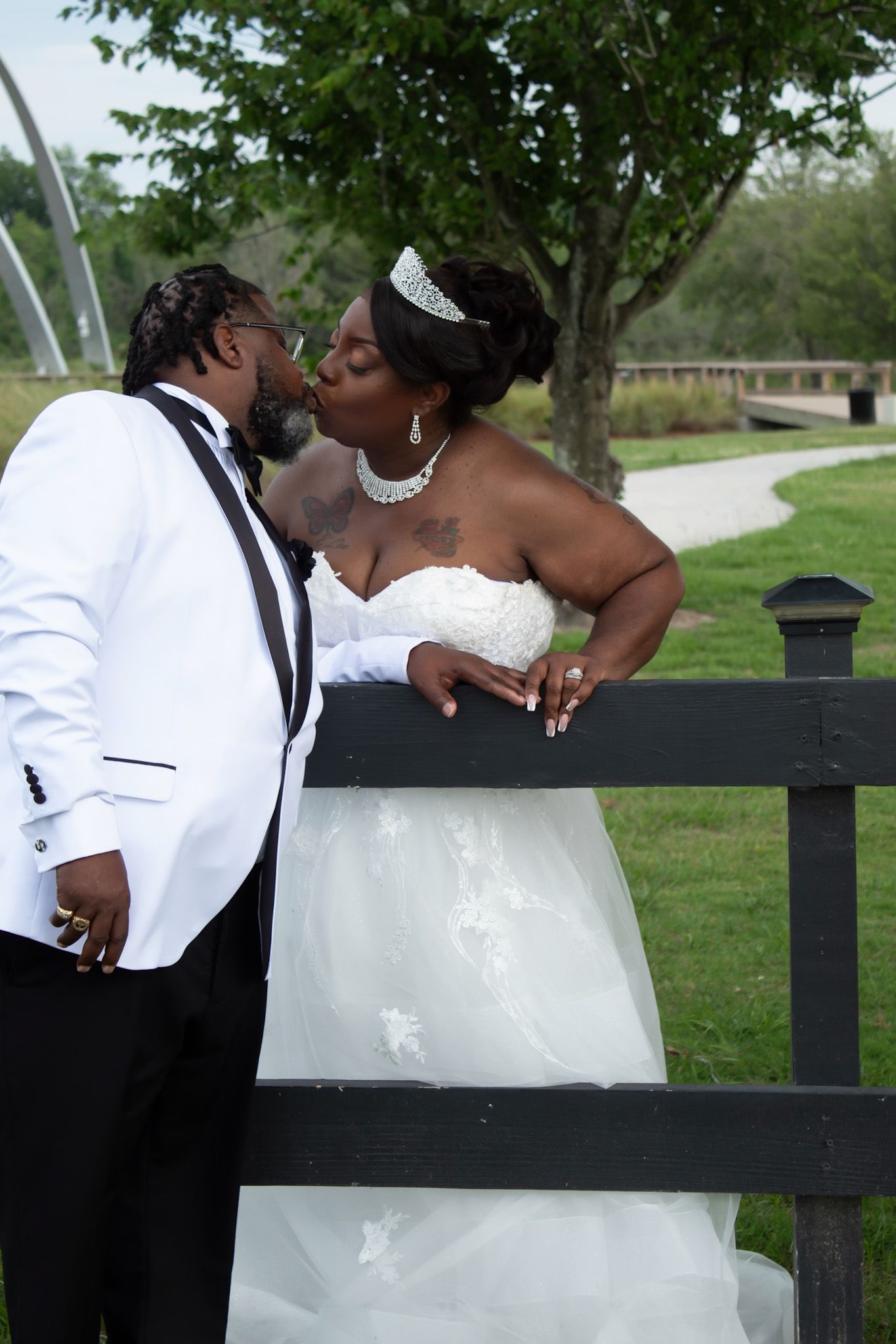 A romantic wedding couple shares a tender kiss while leaning against a black fence in an outdoor garden setting.