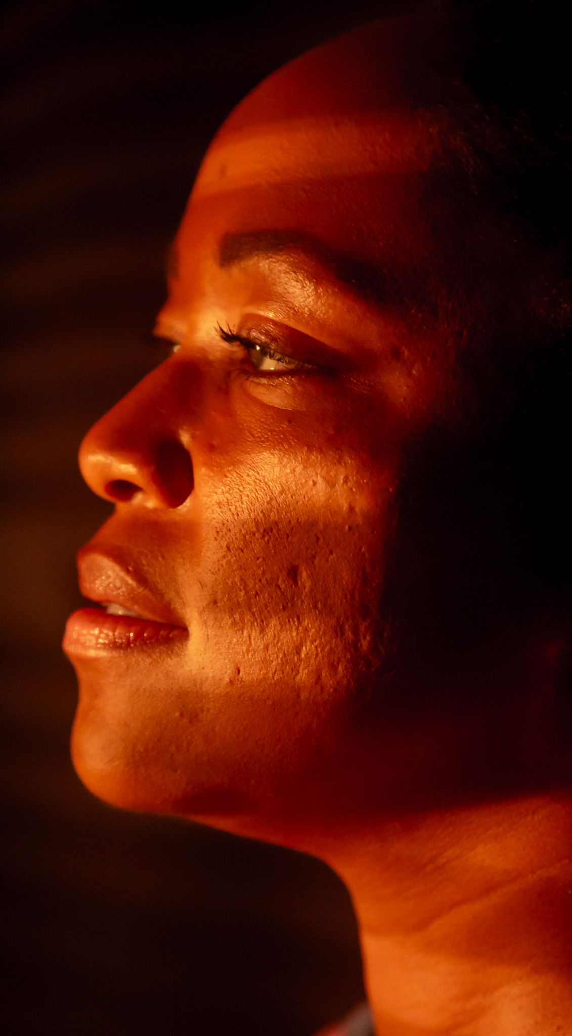 Artistic profile portrait illuminated by warm orange lighting.