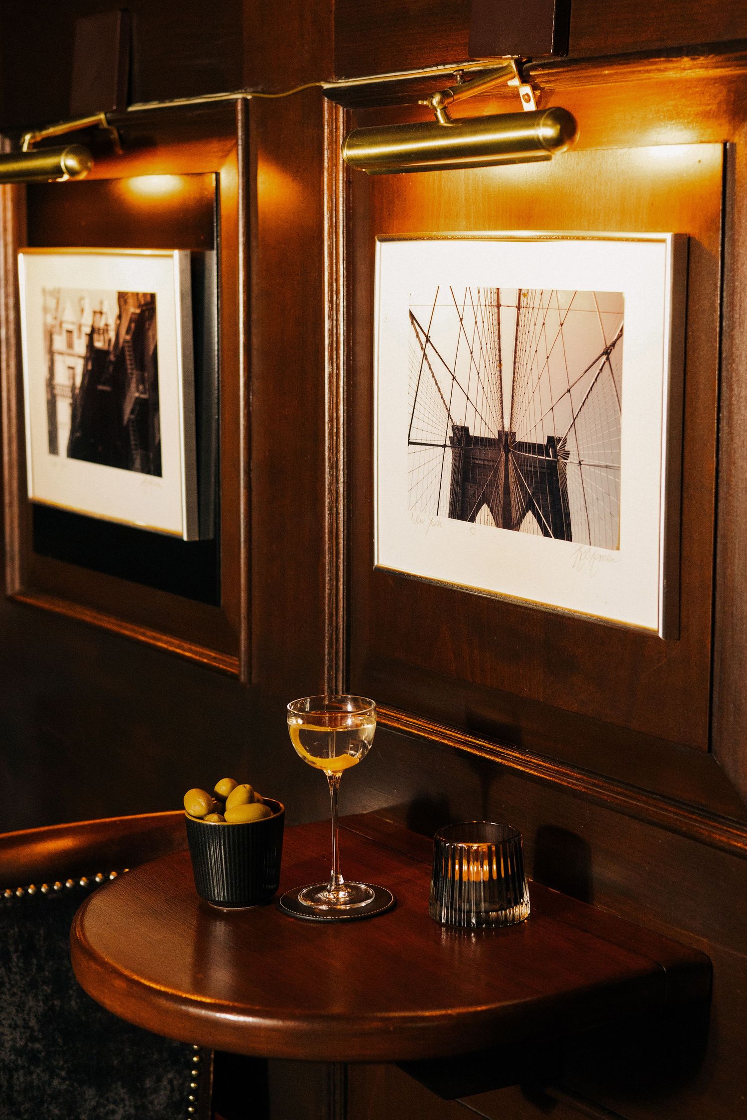 Cozy bar corner with martini glass, olives, framed Brooklyn Bridge art, and warm brass lighting.
