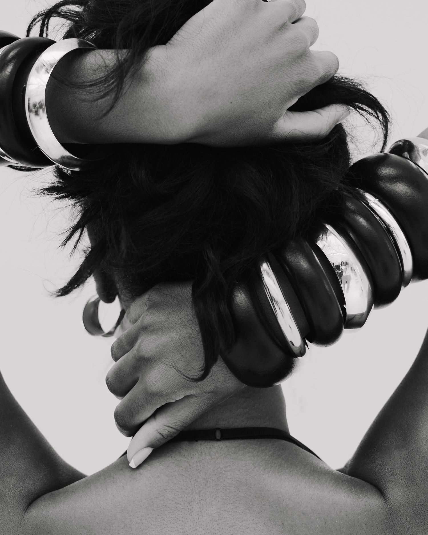 Black and white artistic photo of woman with multiple bangles stacked around her neck and hair.
