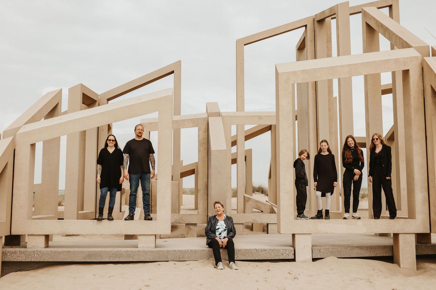 A large family posing inside a wooden house frame structure under an overcast sky at a construction site.