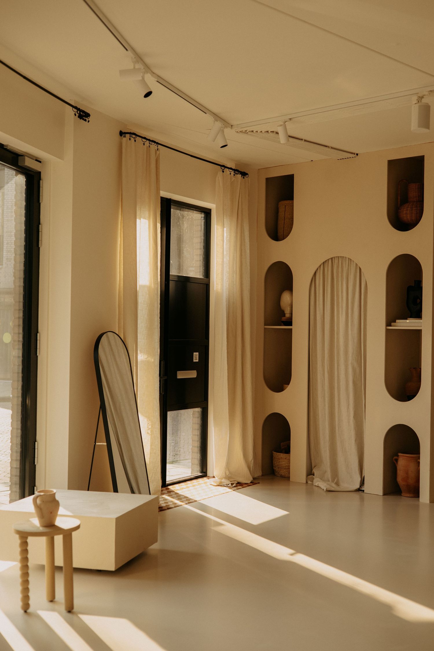 Minimalist boutique interior with cream walls, arched shelving, linen curtains, and natural light.
