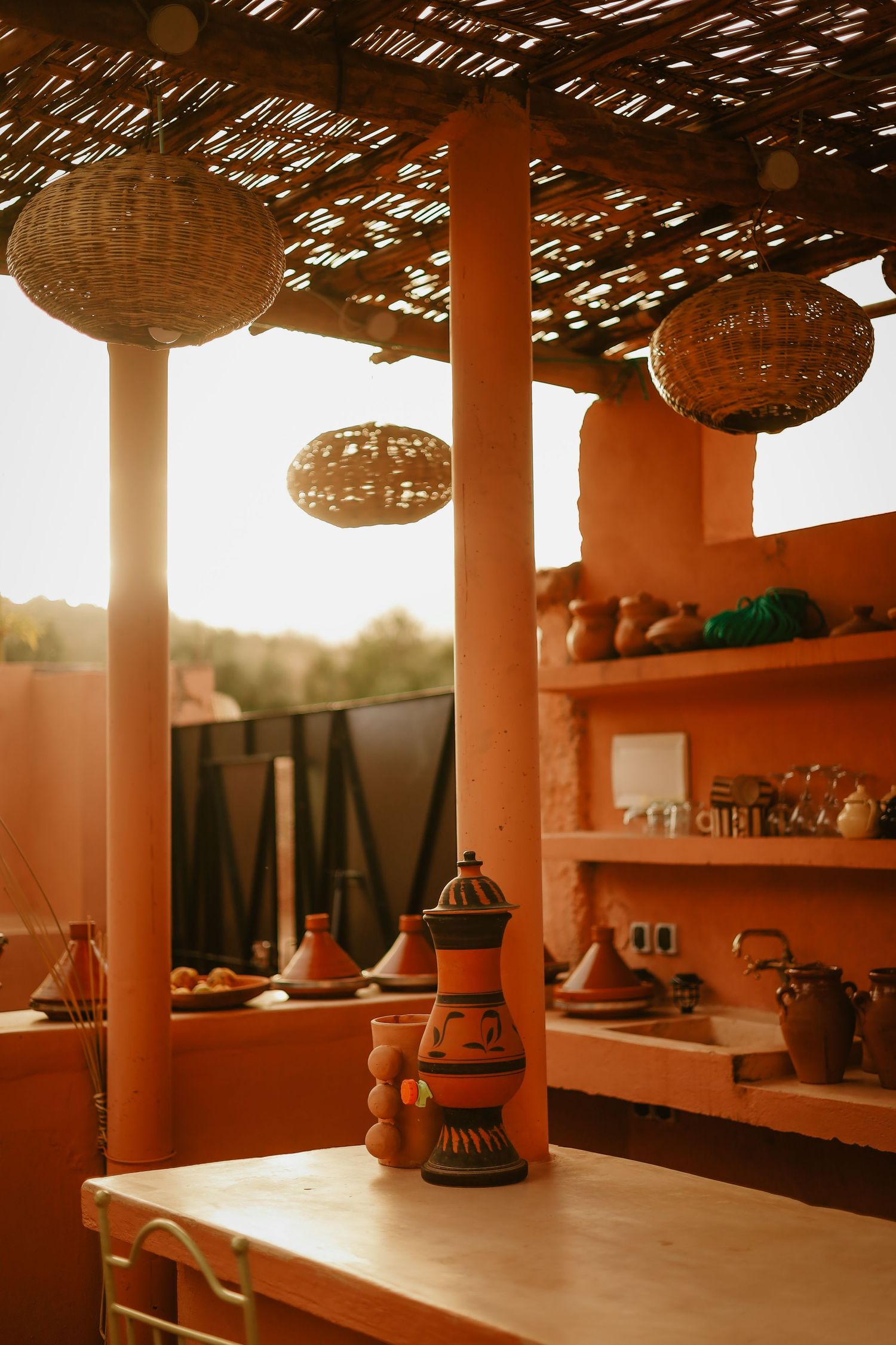 Moroccan terrace kitchen with terracotta walls, wicker pendant lights, and traditional clay pottery.