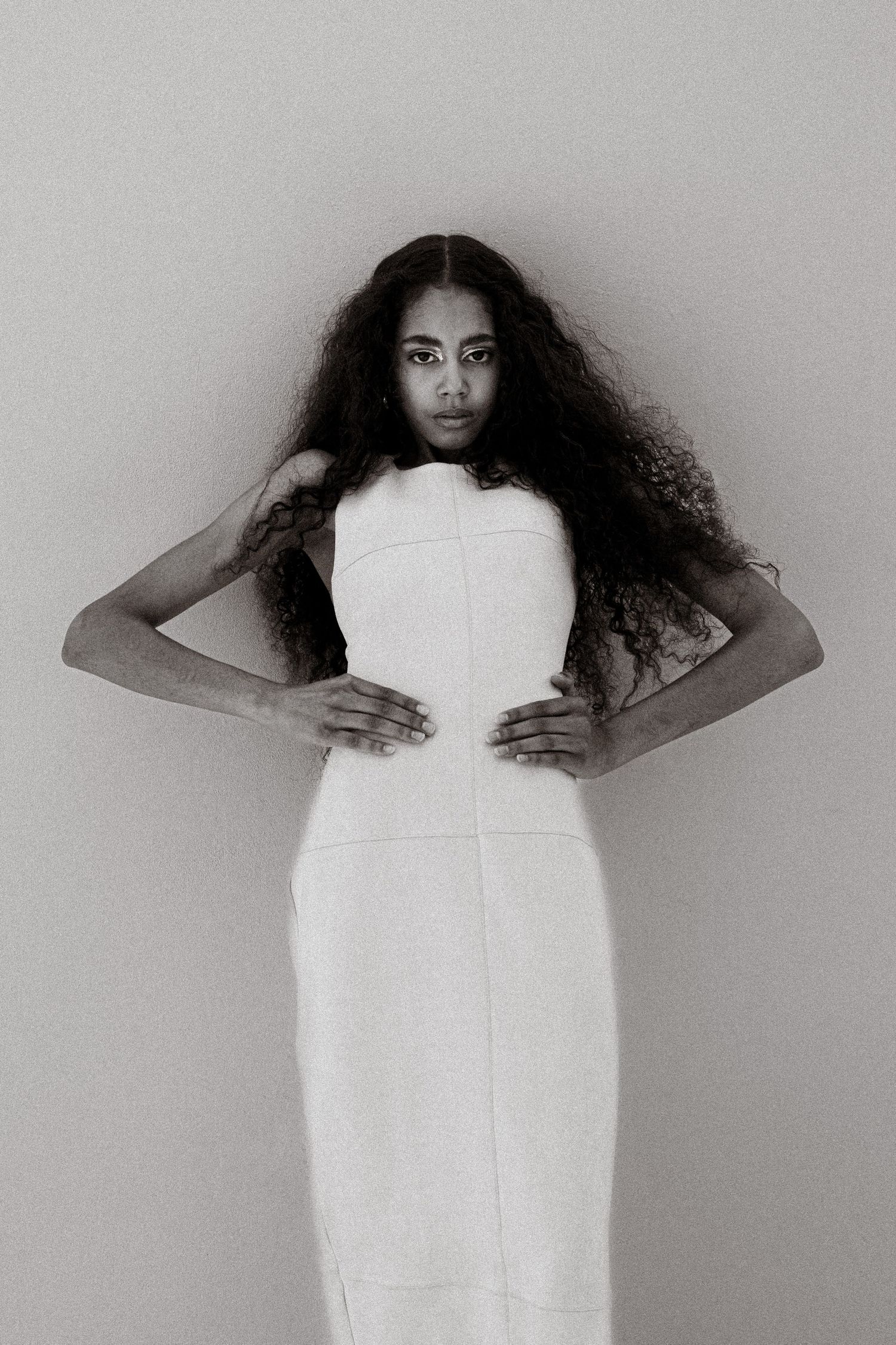 Black and white editorial portrait of woman with voluminous curly hair in structured white dress.