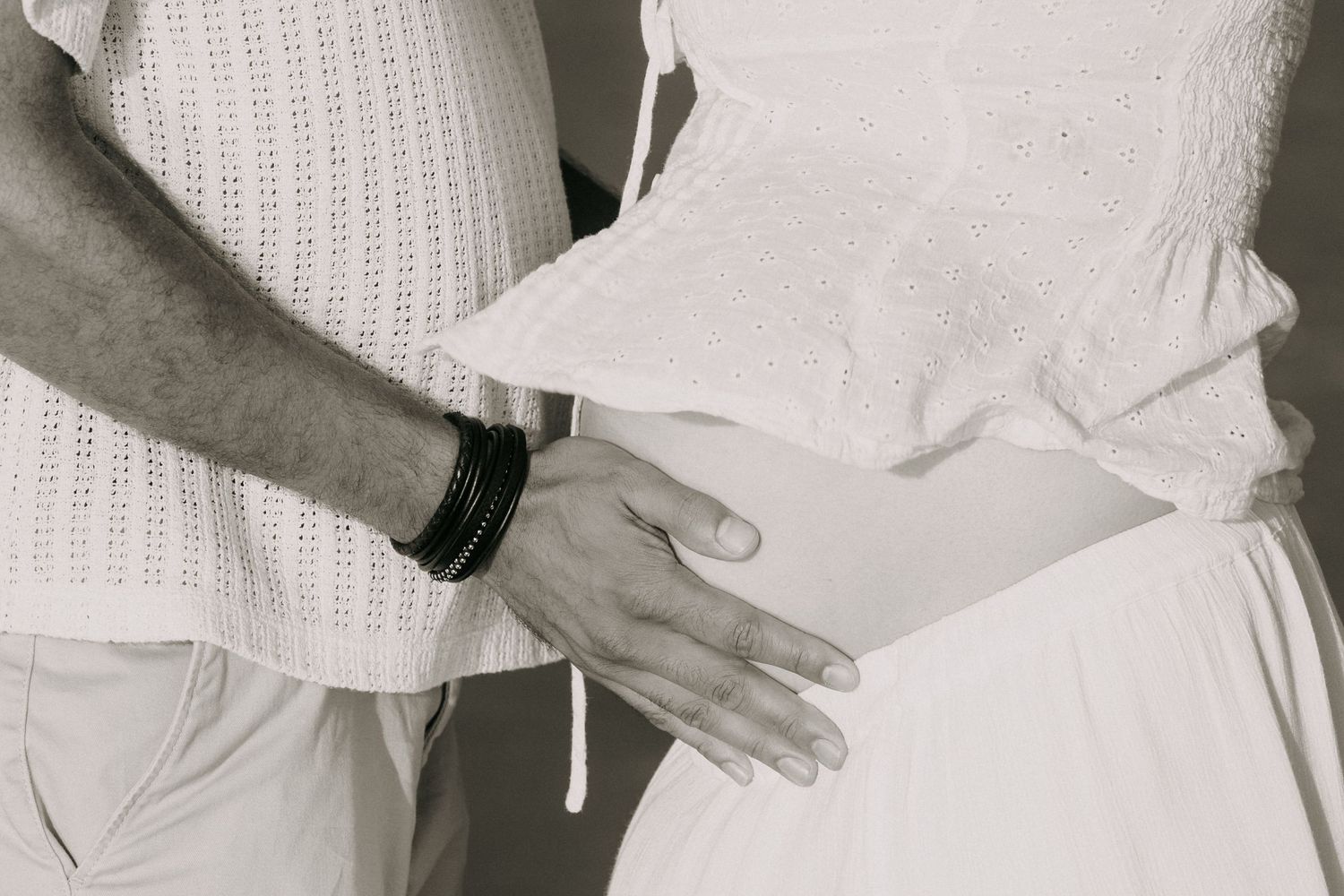 Black and white photo of a couple in white outfits, man placing hand on pregnant woman's belly.
