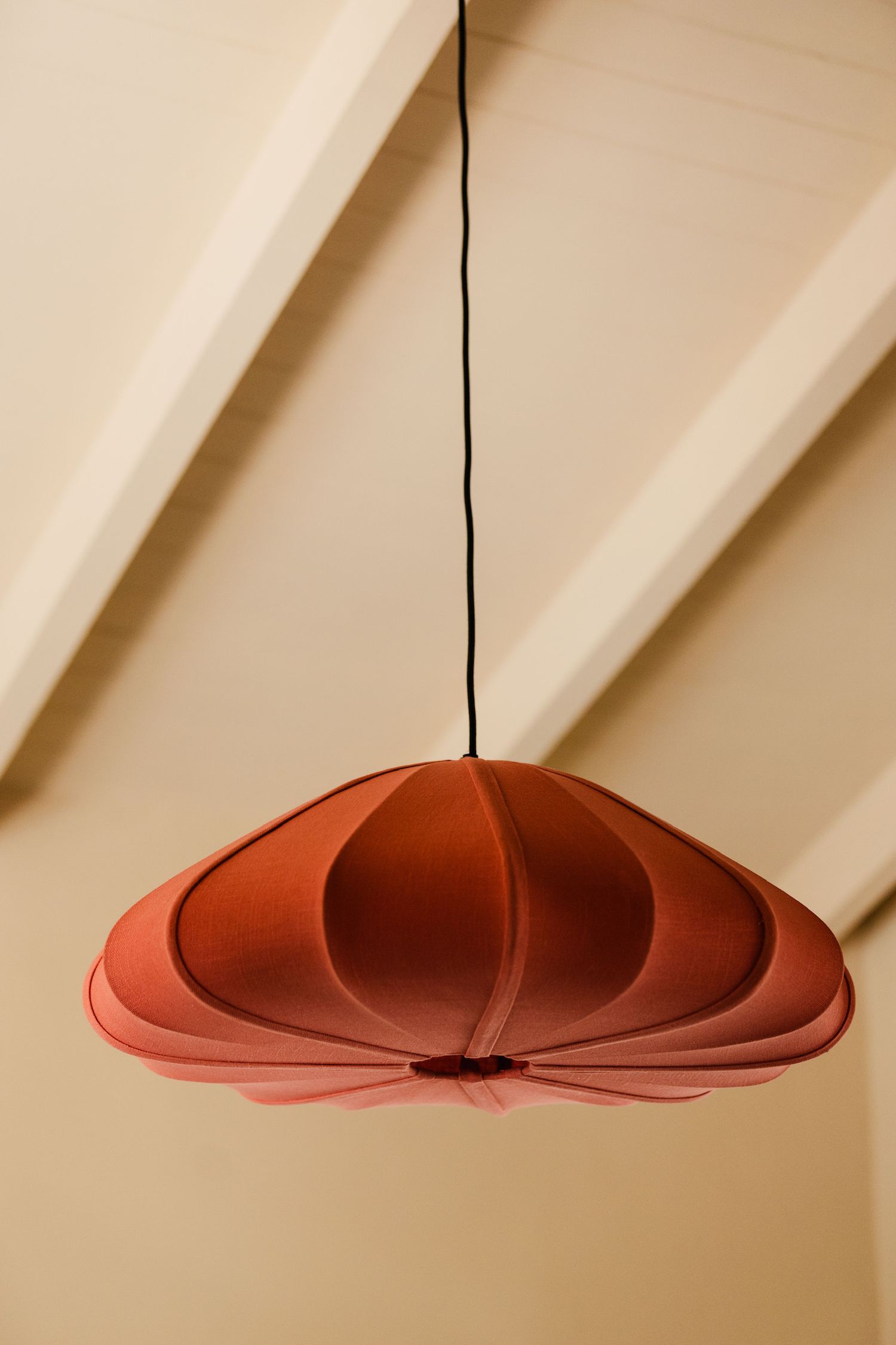 Terracotta red fabric pendant lamp hanging from cream ceiling in stylish interior.