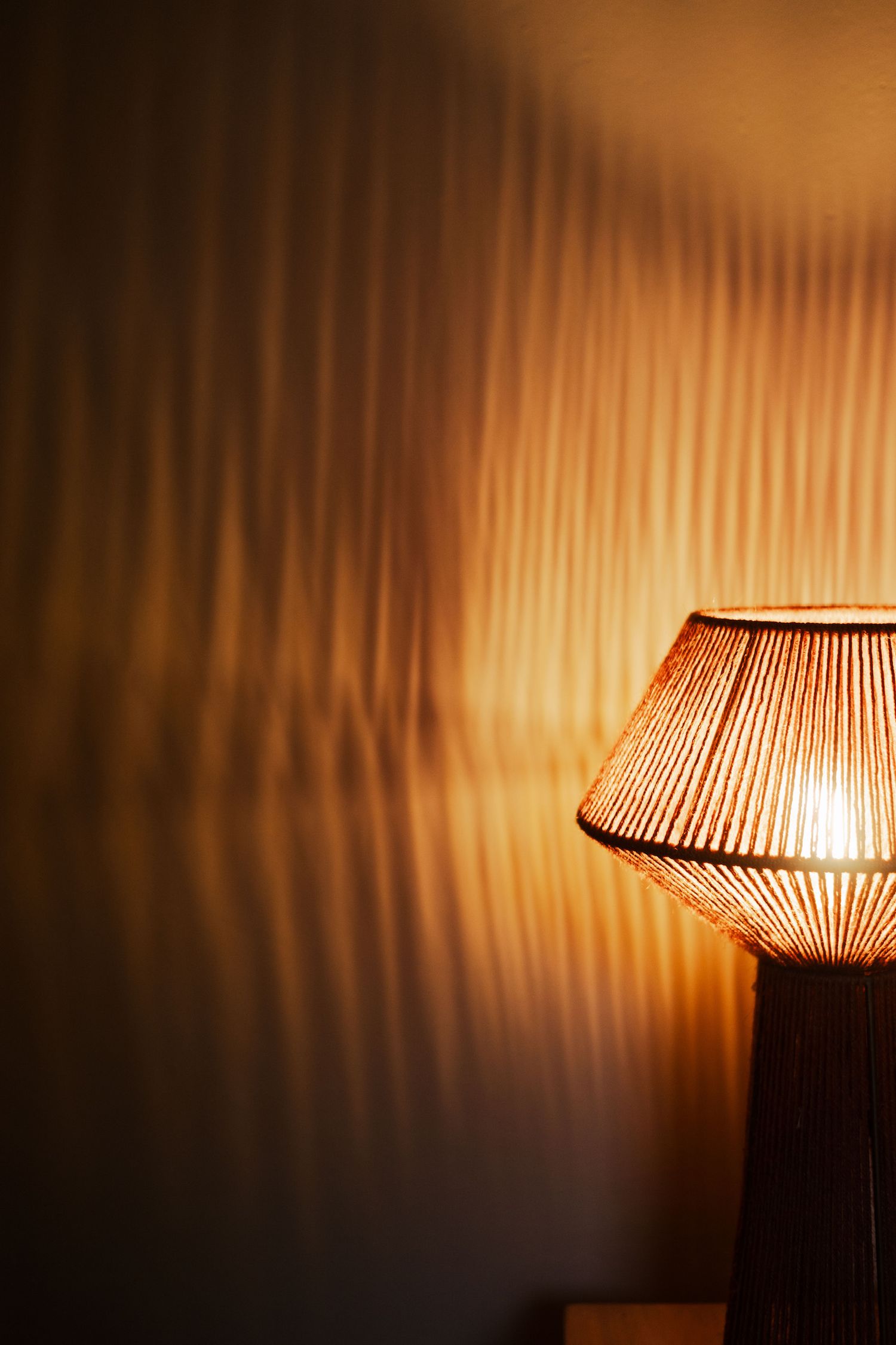 Warm glowing wicker table lamp casting beautiful rippled light patterns on a dark wall.