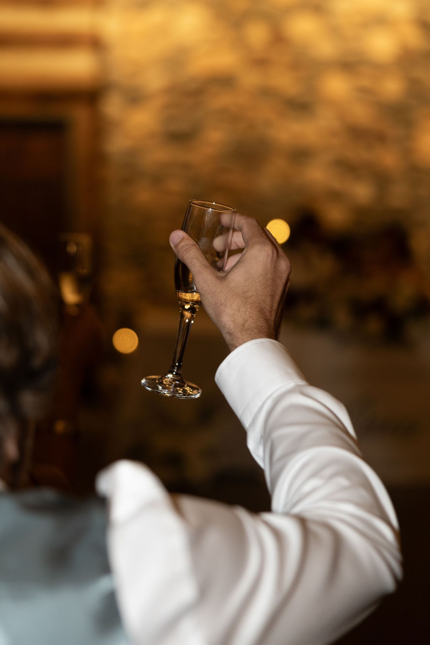 Man in white dress shirt raising an empty champagne flute for a toast at an elegant evening celebration.
