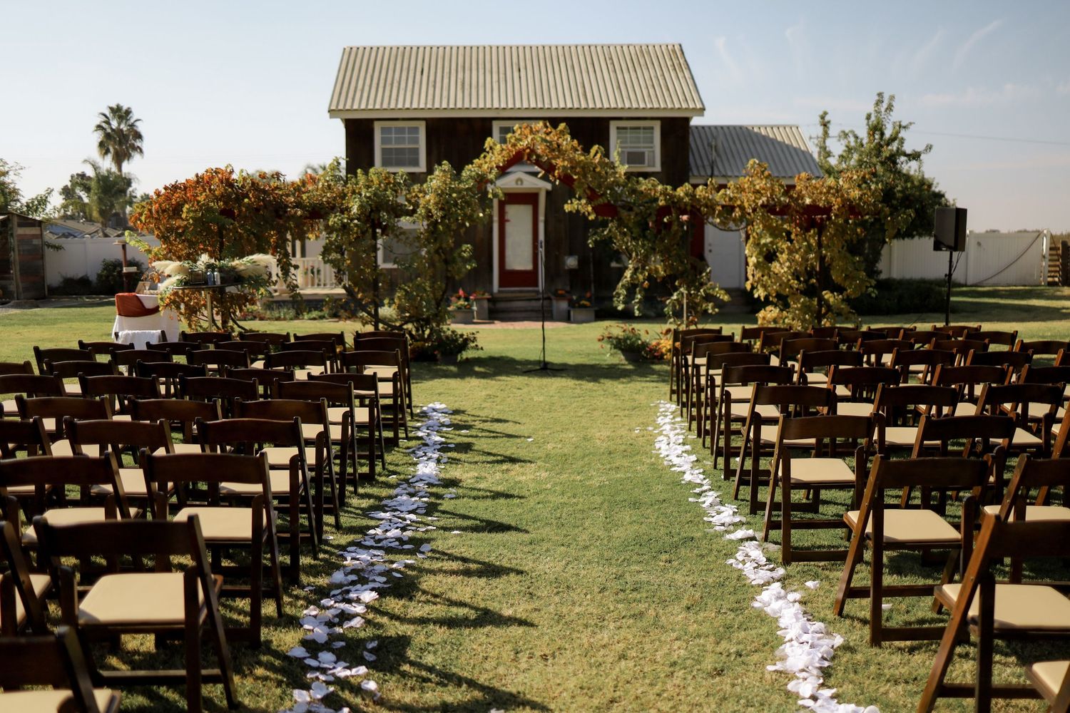 Outdoor wedding ceremony setup with wooden chairs and white aisle runner on a grassy lawn.