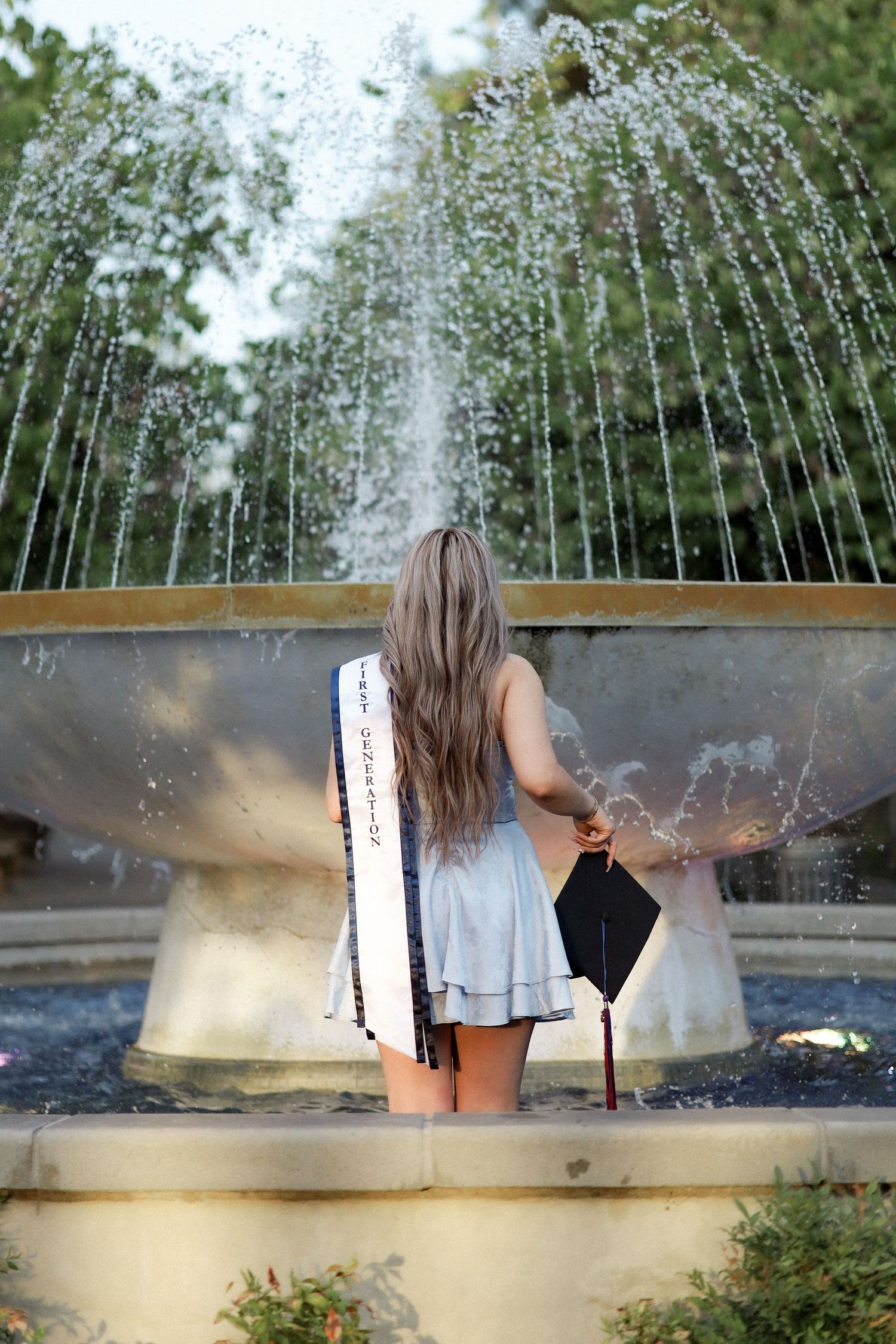 Someone sitting by a water fountain with spraying water jets in a garden setting.