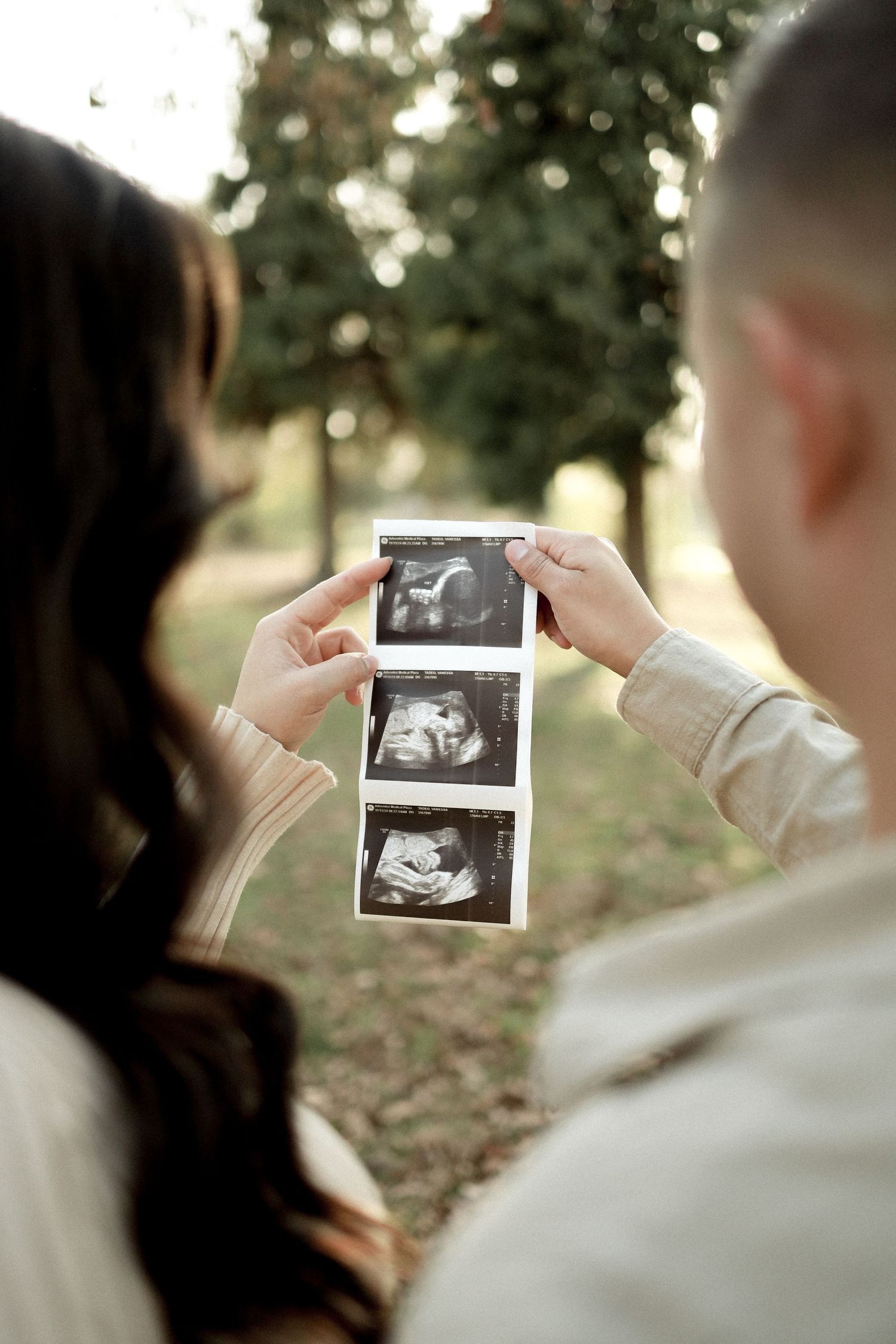 Couple holding ultrasound photos together during an outdoor pregnancy announcement session.