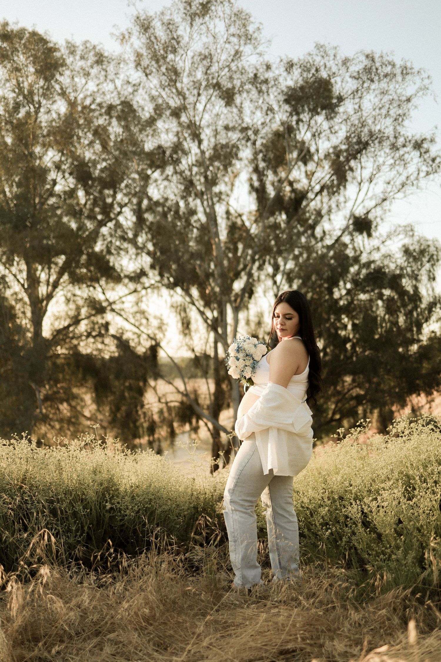 A romantic outdoor photoshoot at sunset in a wildflower field with soft golden light filtering through trees.