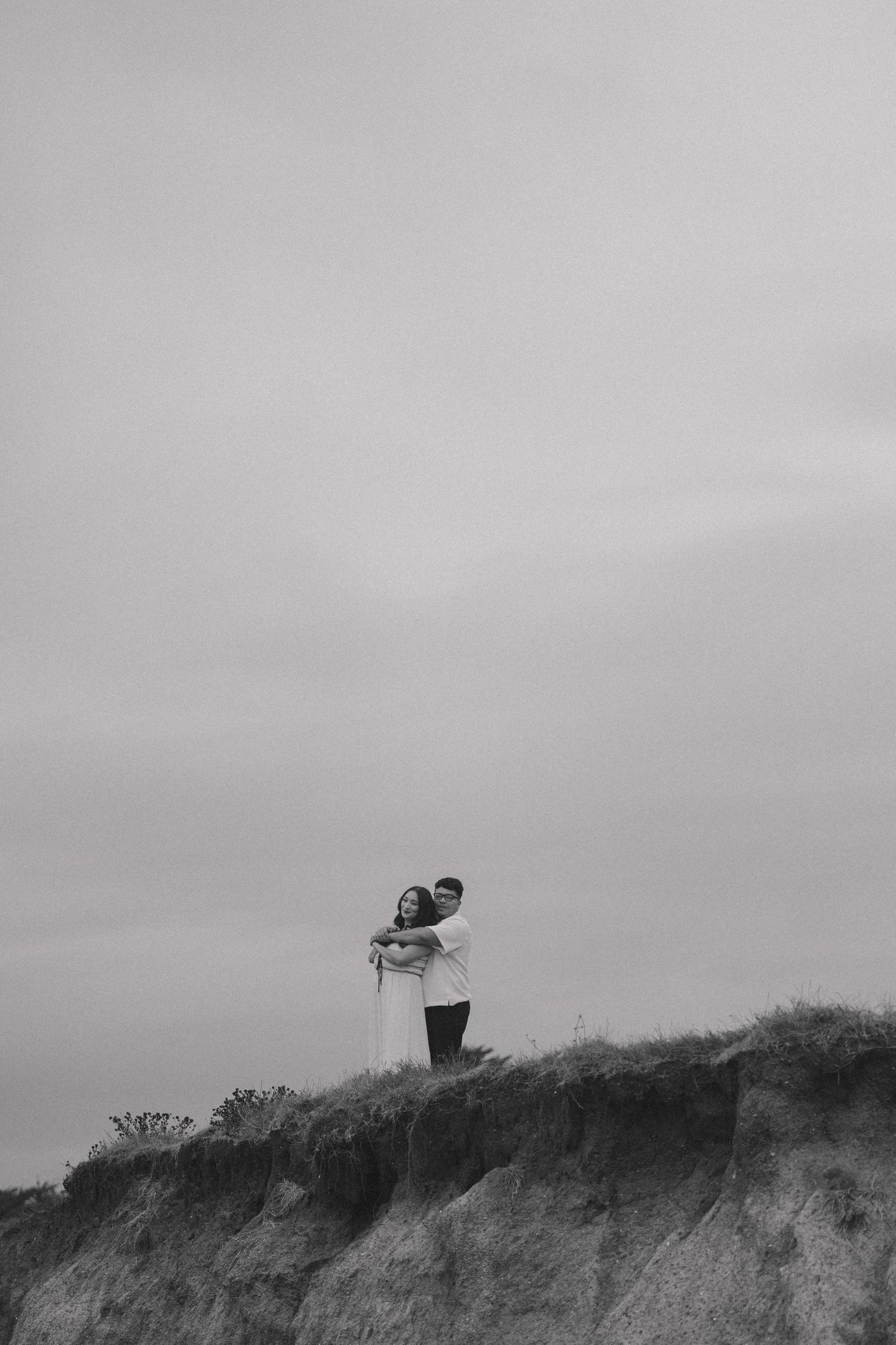 Silhouettes of a couple walking along a hilltop ridge against a moody grey sky.