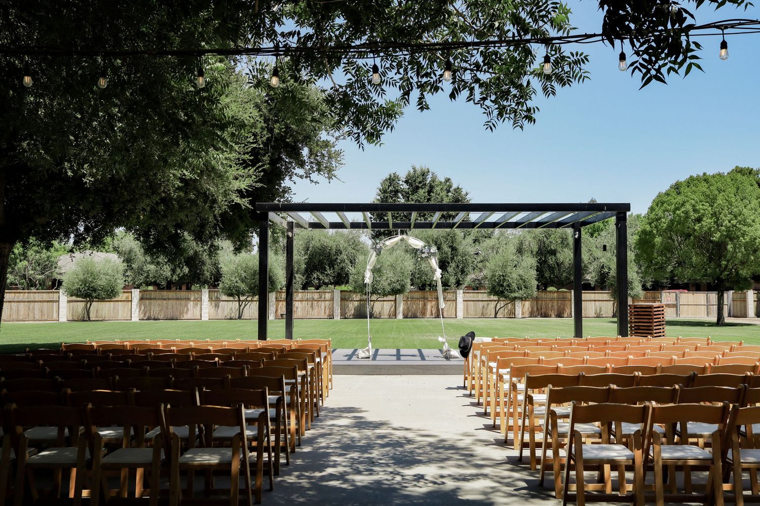 Outdoor wedding ceremony setup with wooden benches and tree-lined aisle.