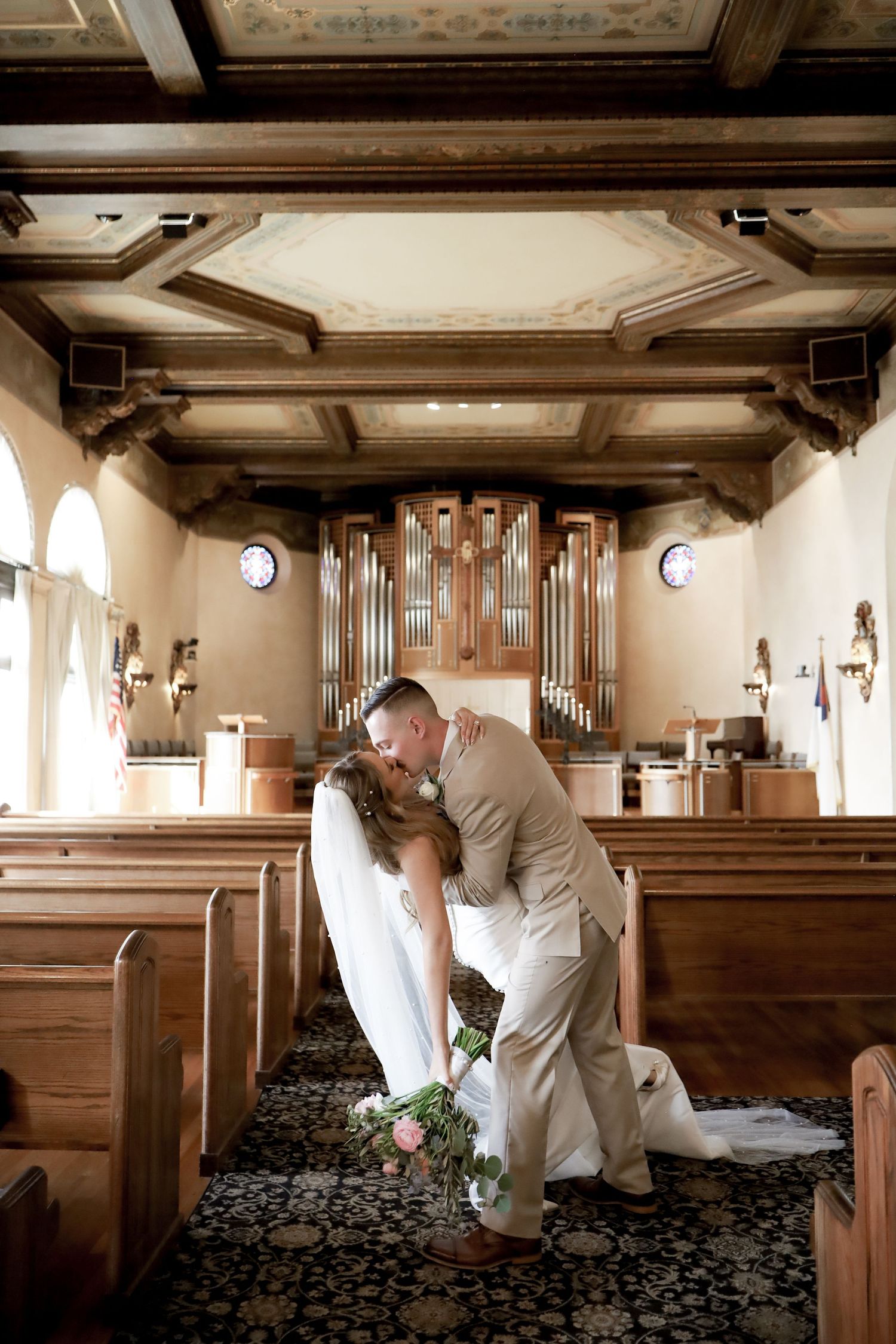 Romantic wedding couple shares intimate moments in a church sanctuary with wooden pews and organ pipes.
