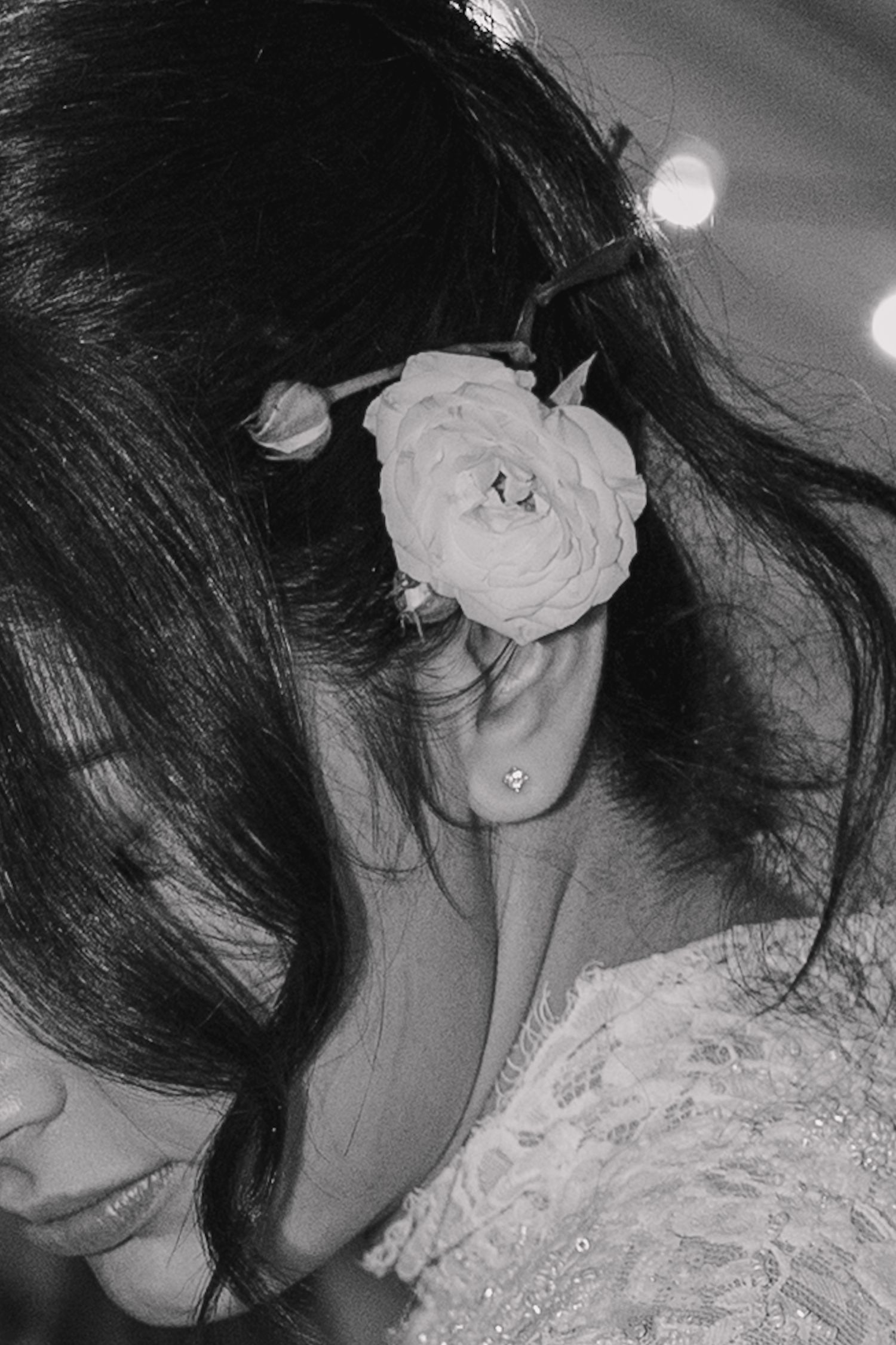 Black and white portrait of a bride with a rose flower hair accessory and diamond stud earring, smiling softly.