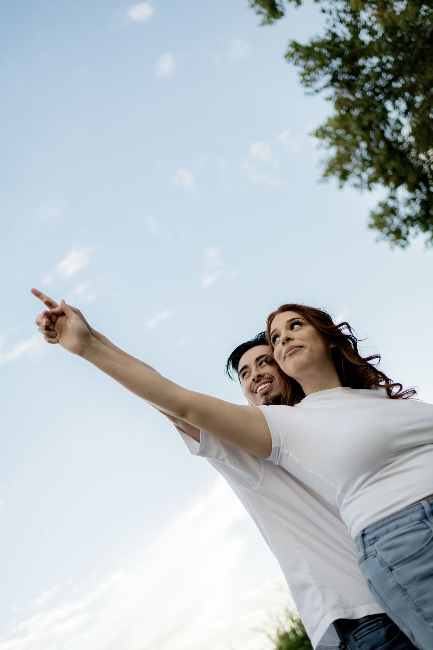 Person in white shirt and jeans twirling joyfully against a bright blue sky with trees in the background.