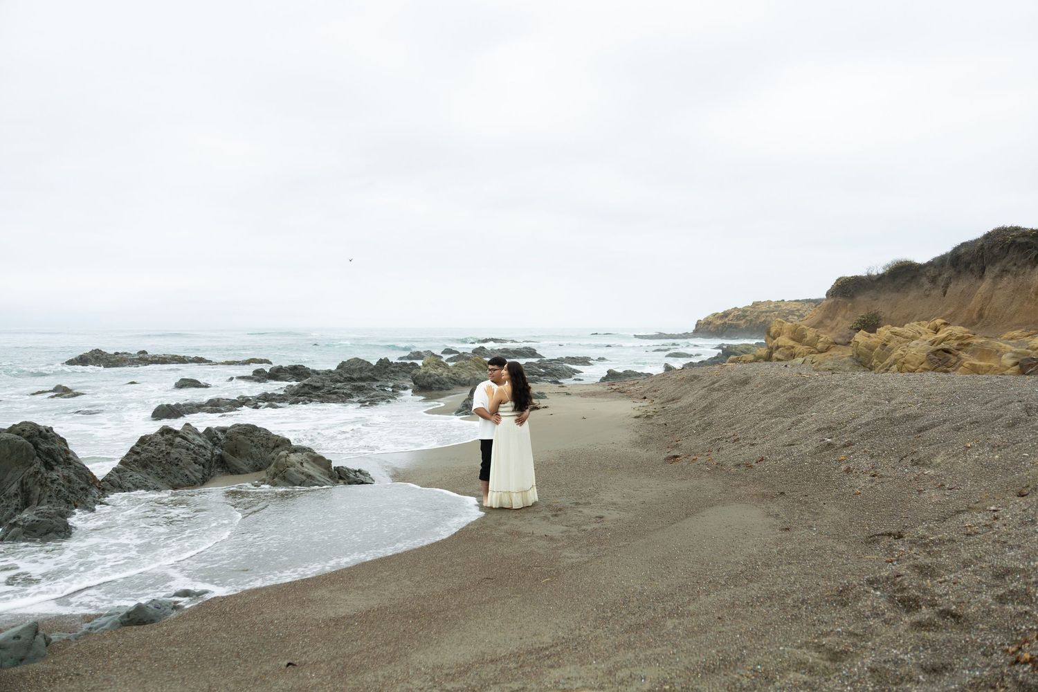 Dramatic coastal landscape with waves crashing against rocky shore under overcast skies.