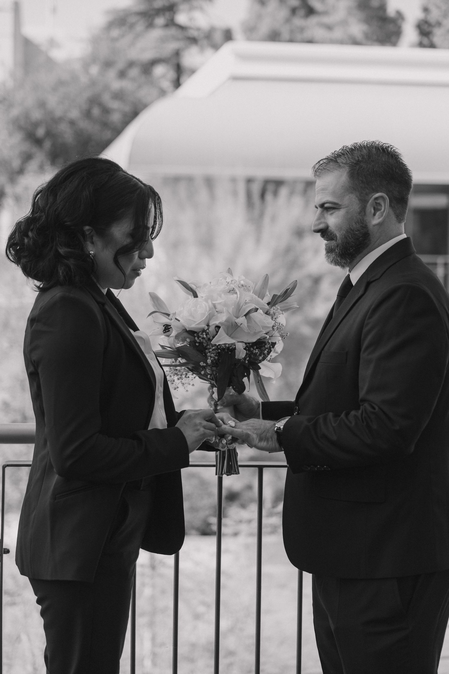 Wedding party members in black suits reading from papers during an outdoor ceremony.