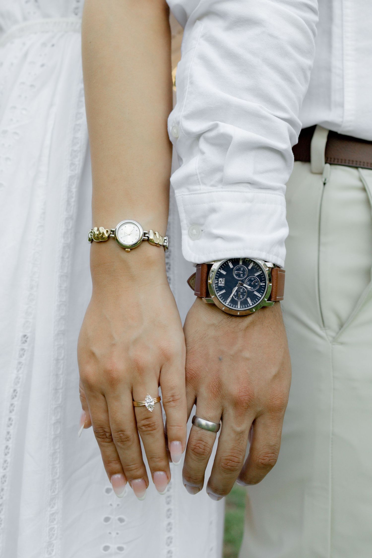 Close-up of two hands wearing wedding rings and watches against white clothing background.